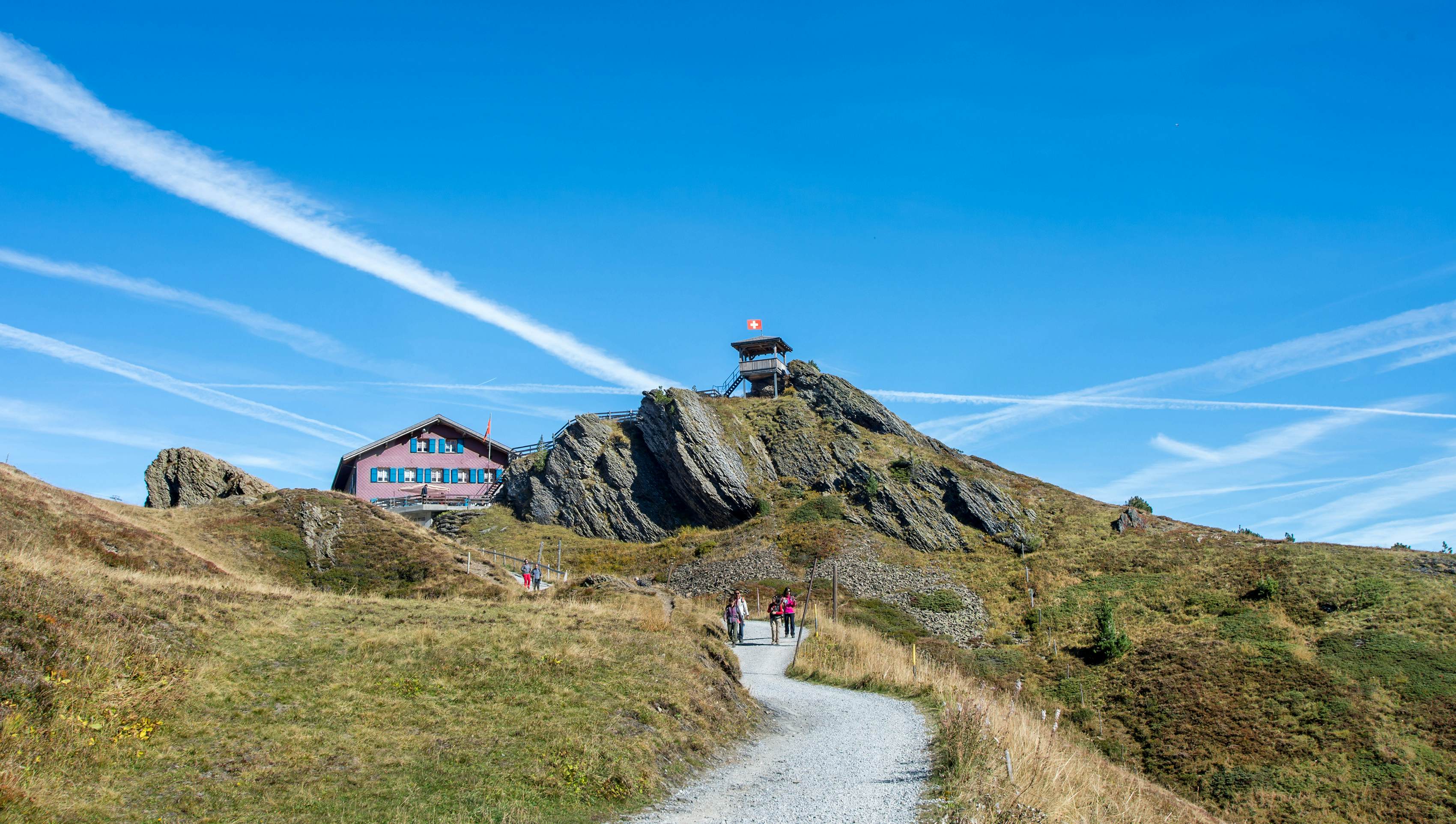 People follow a mountain trail on a sunny day up to a mountain viewpoint