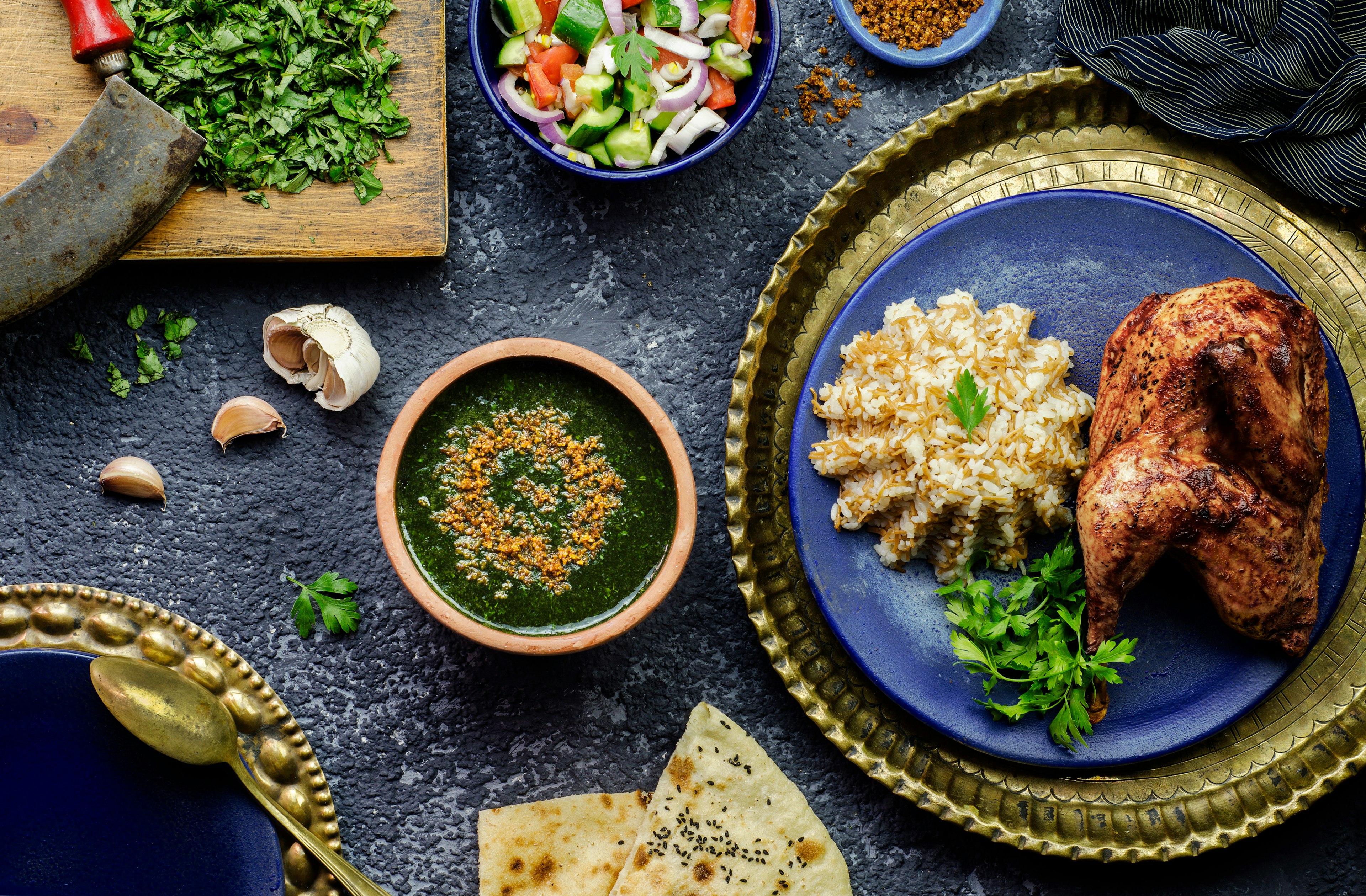 Arabic cuisine; Egyptian dish Molokhya or Molokhia placed with rice, chicken, pita bread, oriental green salad, crispy fried garlic and fresh ingredients on rustic background.