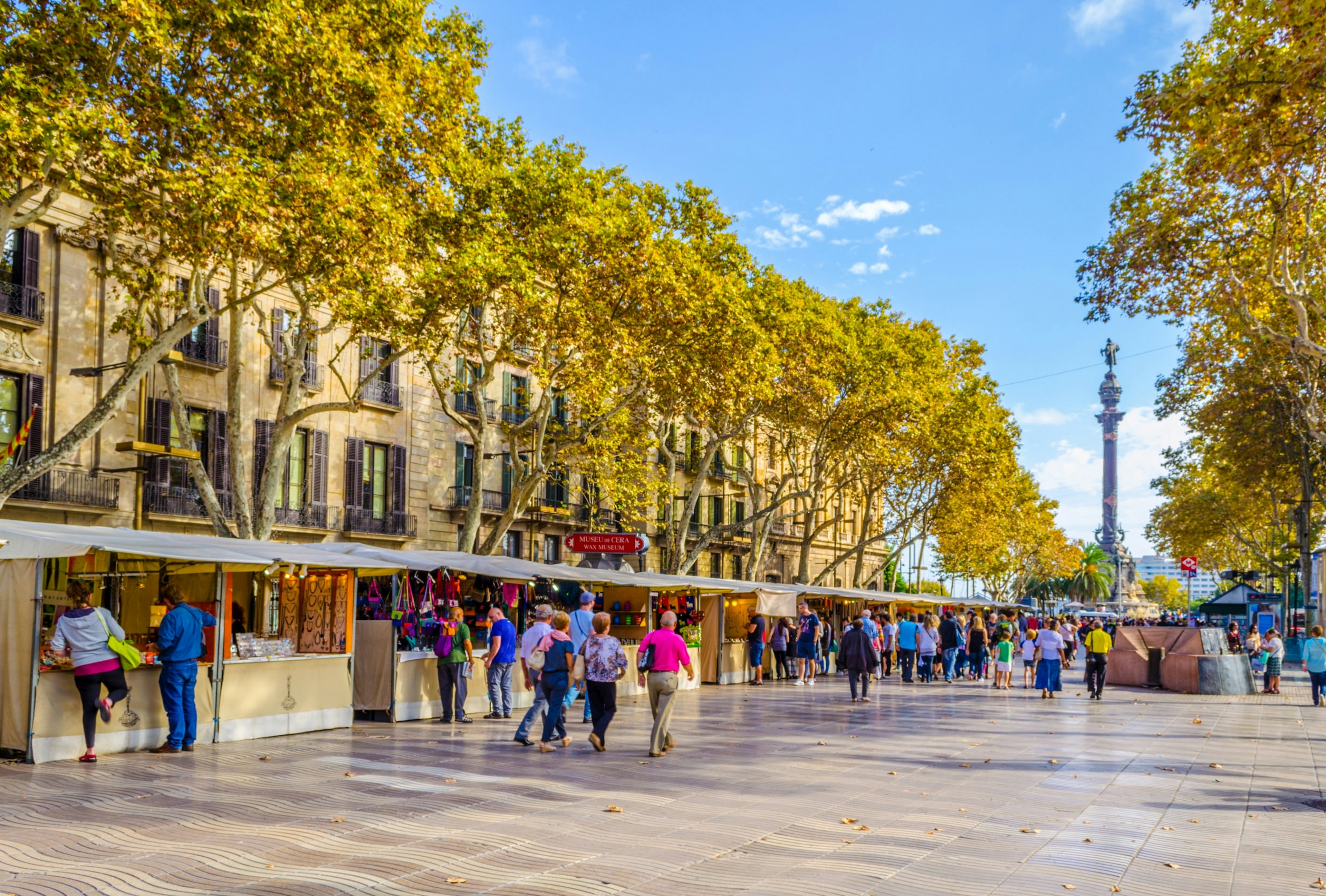 Bright blue skies over shoppers browsing market stalls on tree-lined La Rambla: one of the essential free things to do in Barcelona.