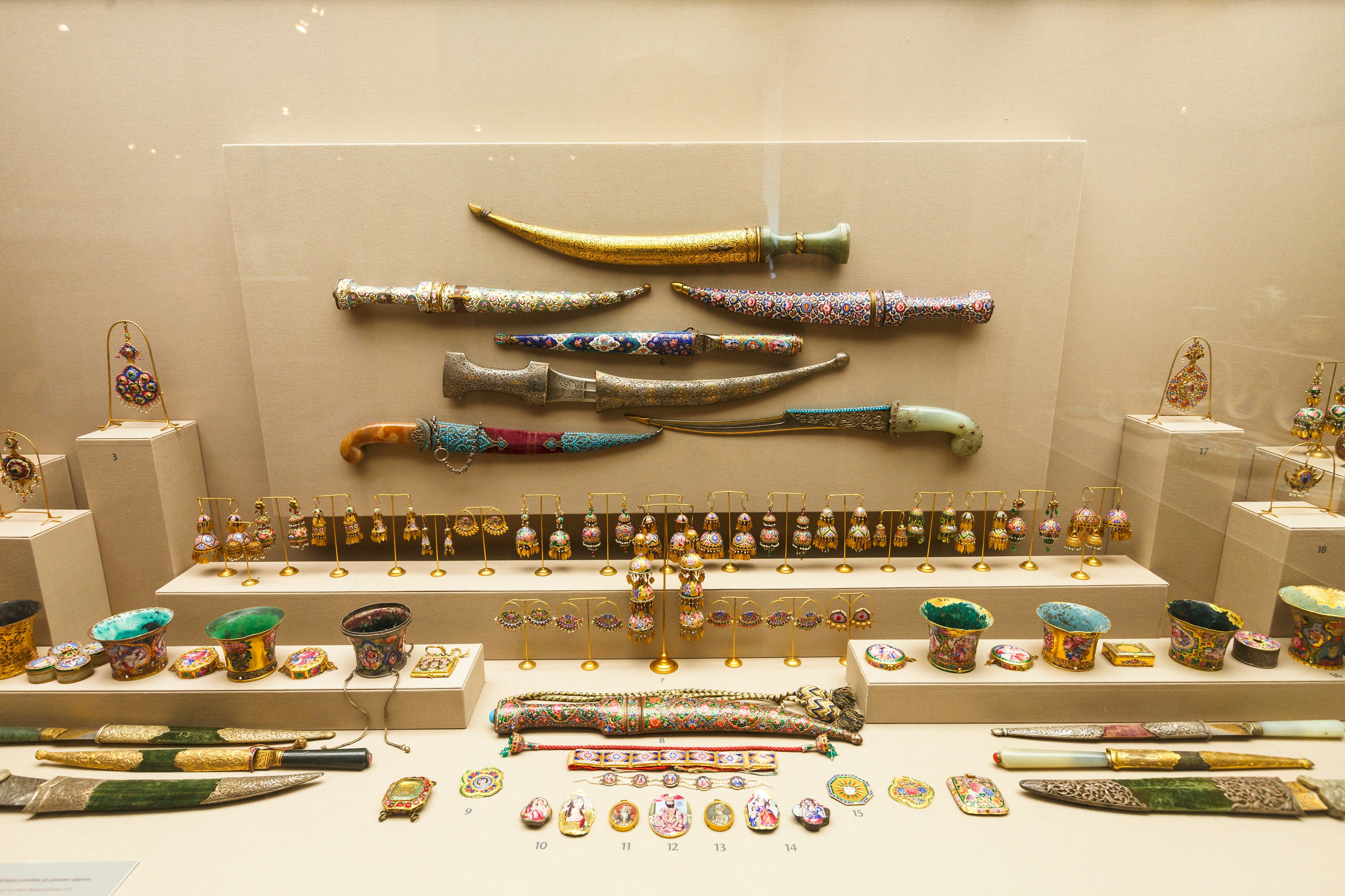 A broad display of jewellery and daggers, many with intricate patterns. Colours are predominantly gold, blue and red.