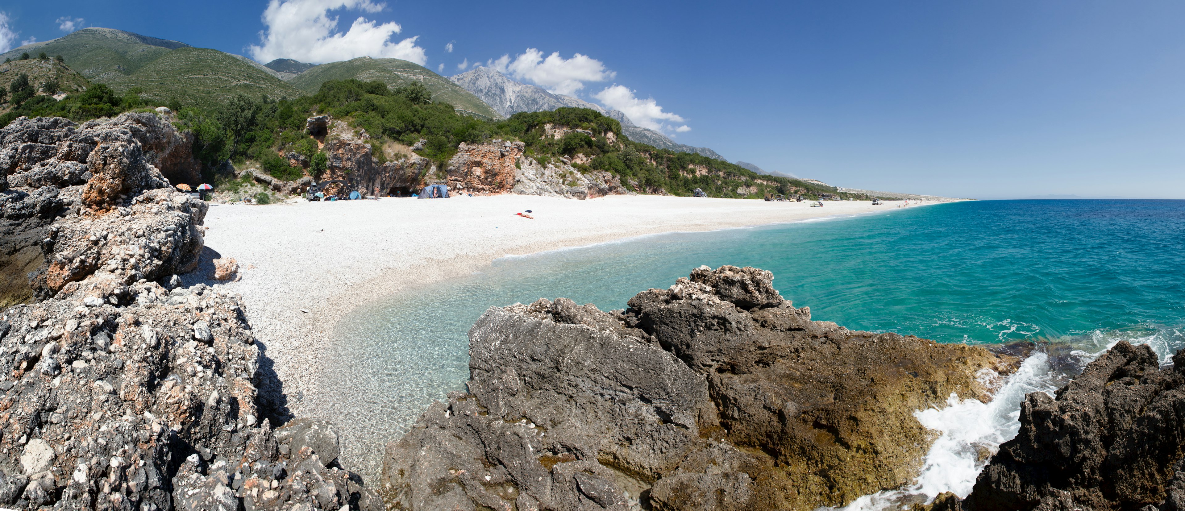 Pebbly Palasa beach with green hills behind it and mountains in the distance.