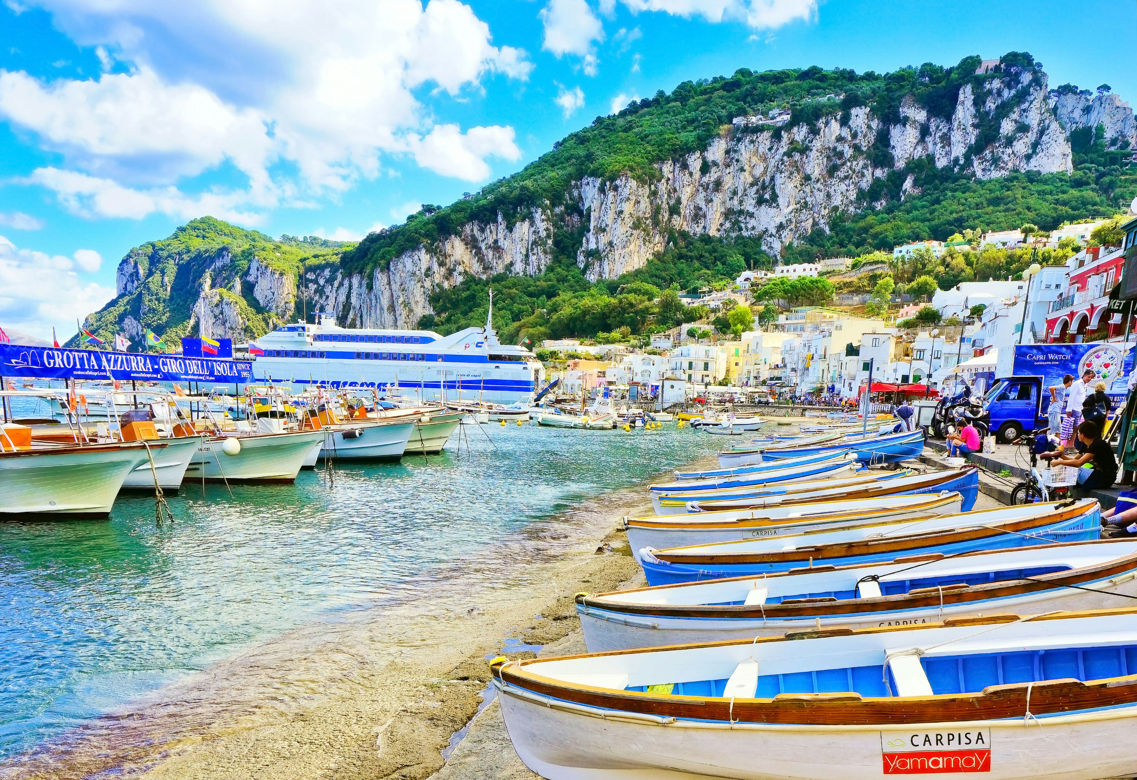 Sparkling water laps at the beach, which is lined with small white and blue boats.