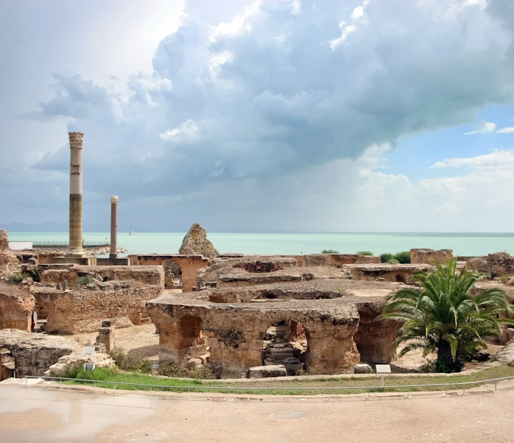 The image looks across a series of thick stone arches and two stone columns towards the sea, which has a thick thunder cloud over it.
