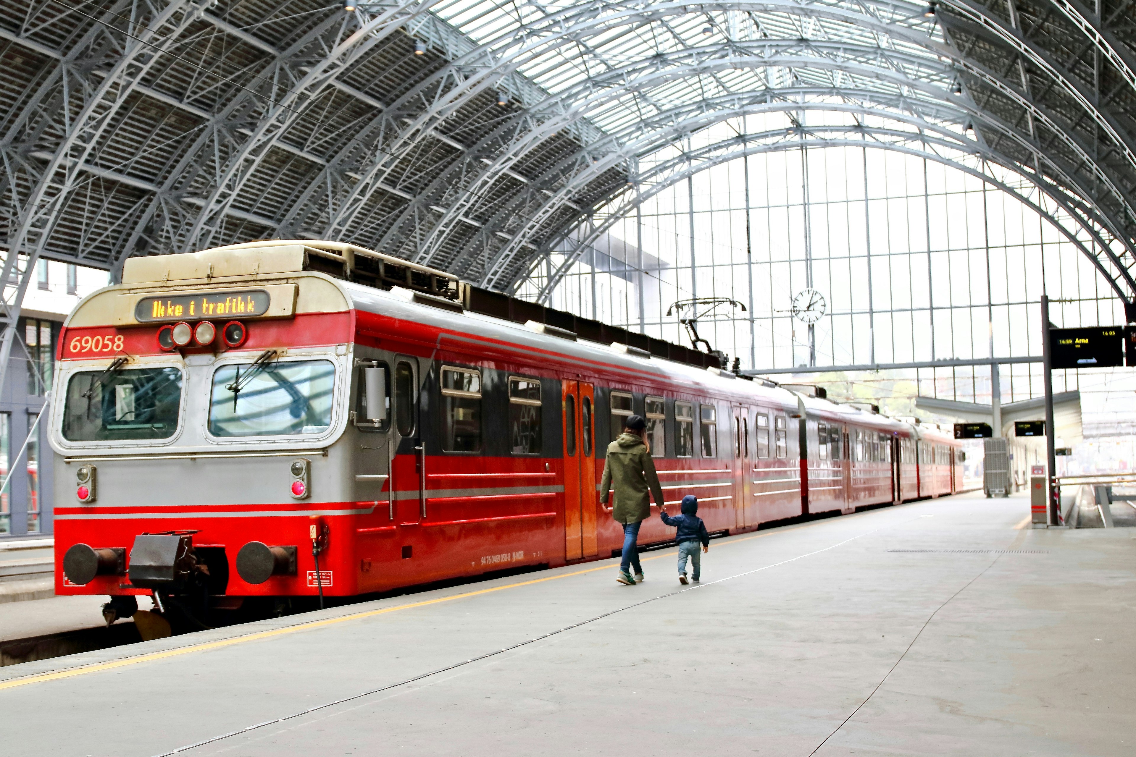 Two people, a mother and child, walk towards a red train waiting on a platform at Bergen's train station, Norway