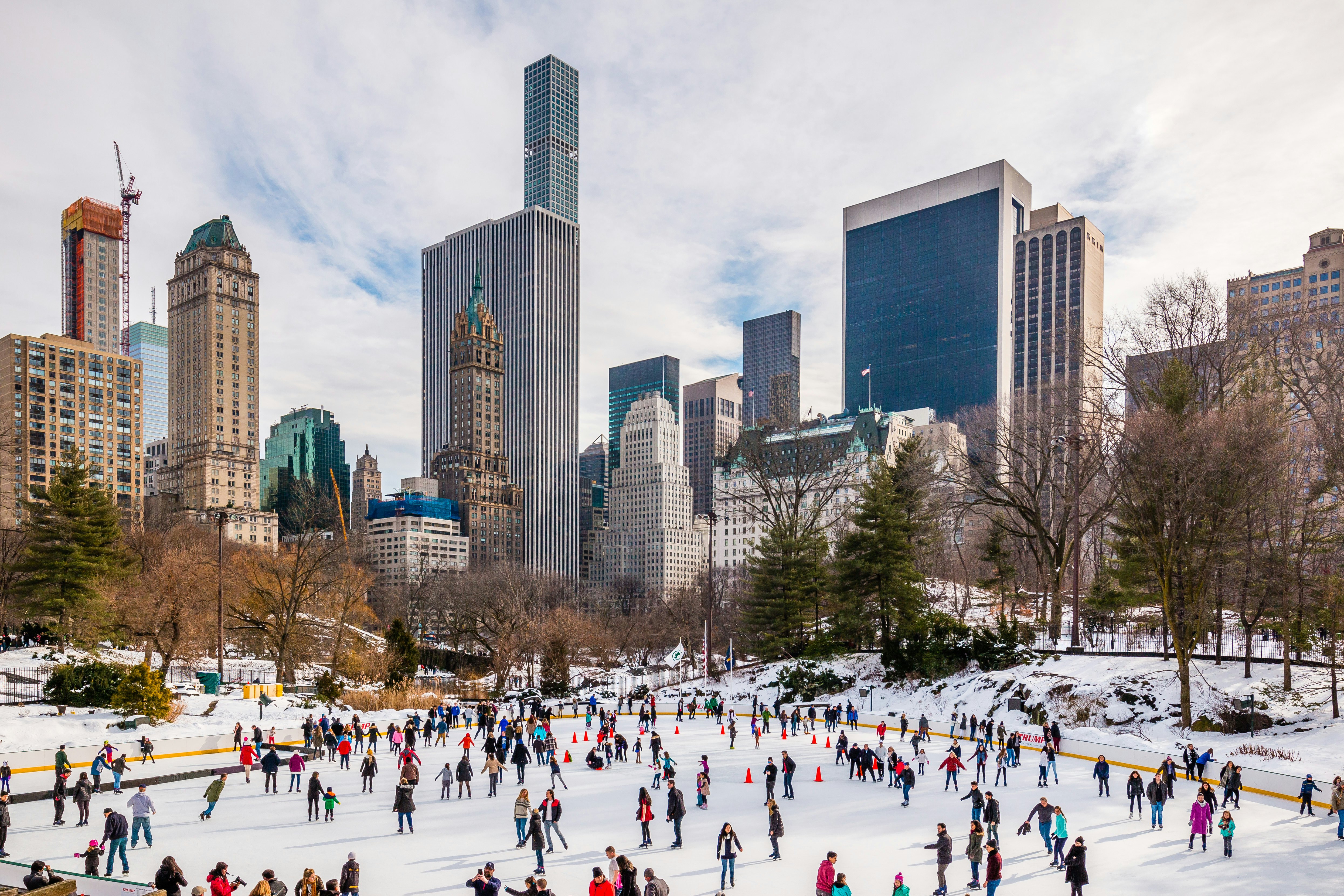 Ice skaters wrapped up on winter gear on an ice rink in the shadow of high-rise buildings