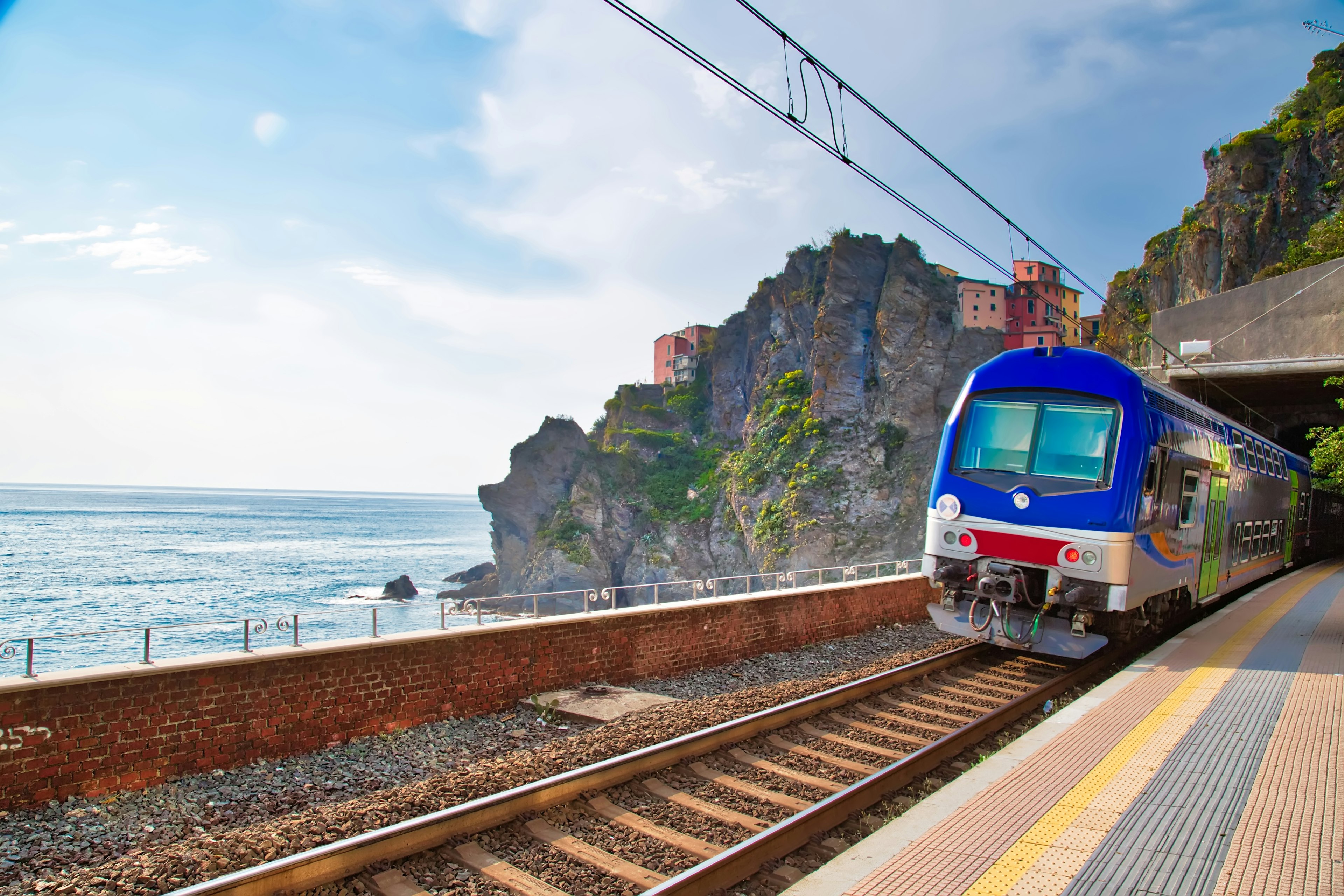 A blue train passes through Manarola Train Station in Italy