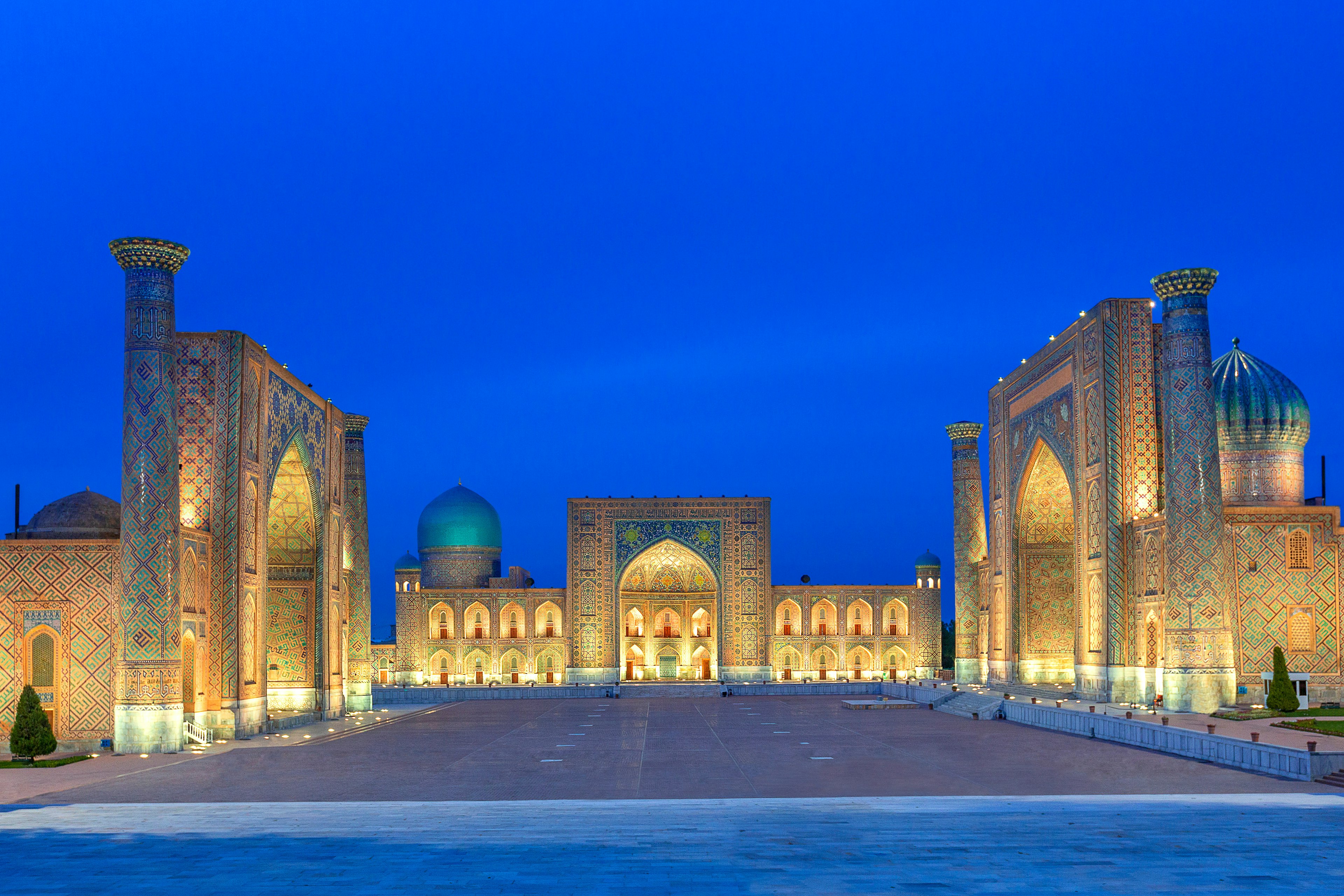 The tiled facades of the Registan square uplight in the evening, with a dark blue evening sky