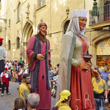 Colourful giants parading through La Rambla during La Mercè festival; the giants are made from papier-mâché and wear traditional religious dress, while onlookers watch the procession.