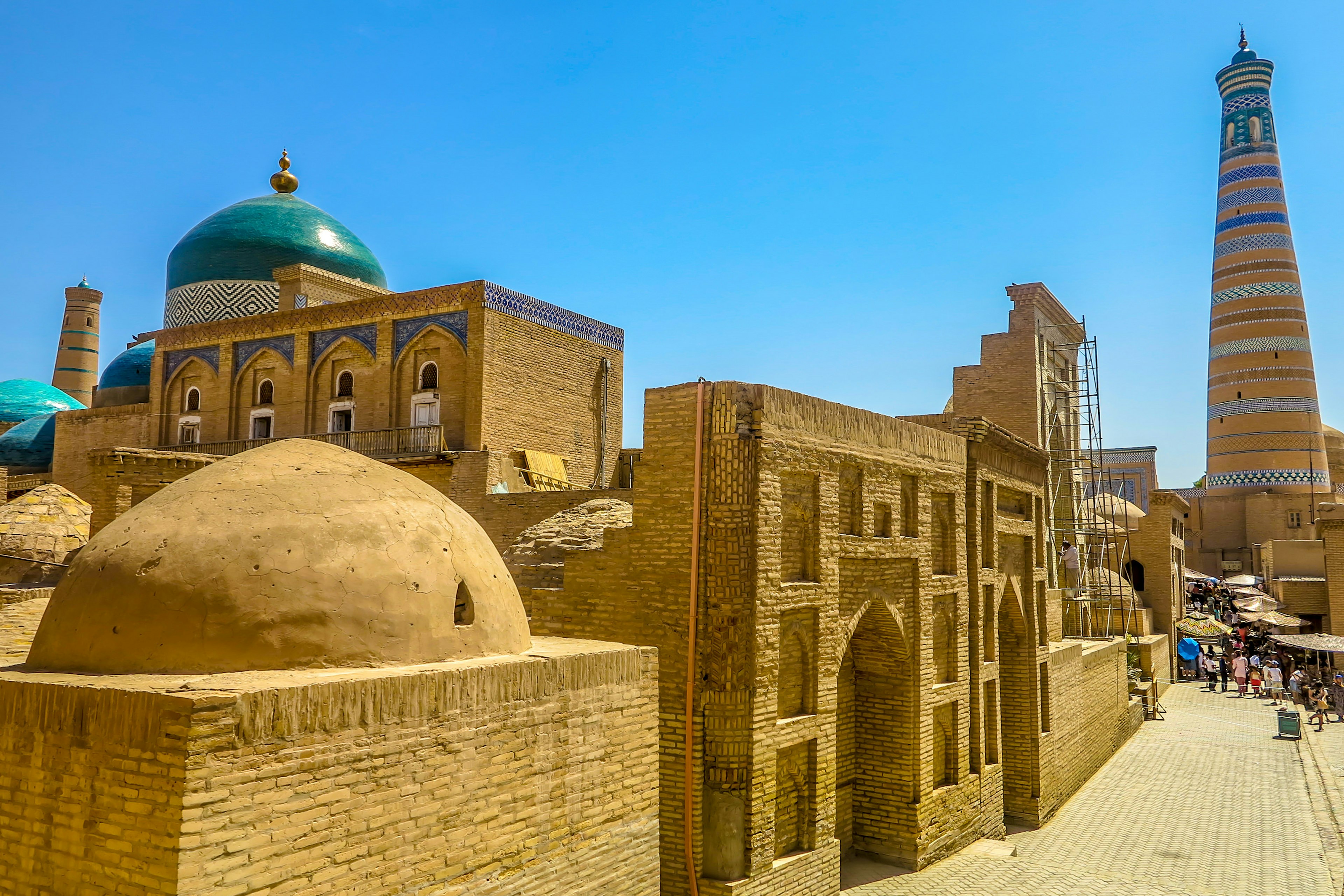 Mud brick structures with blue domes and visitors walking the streets