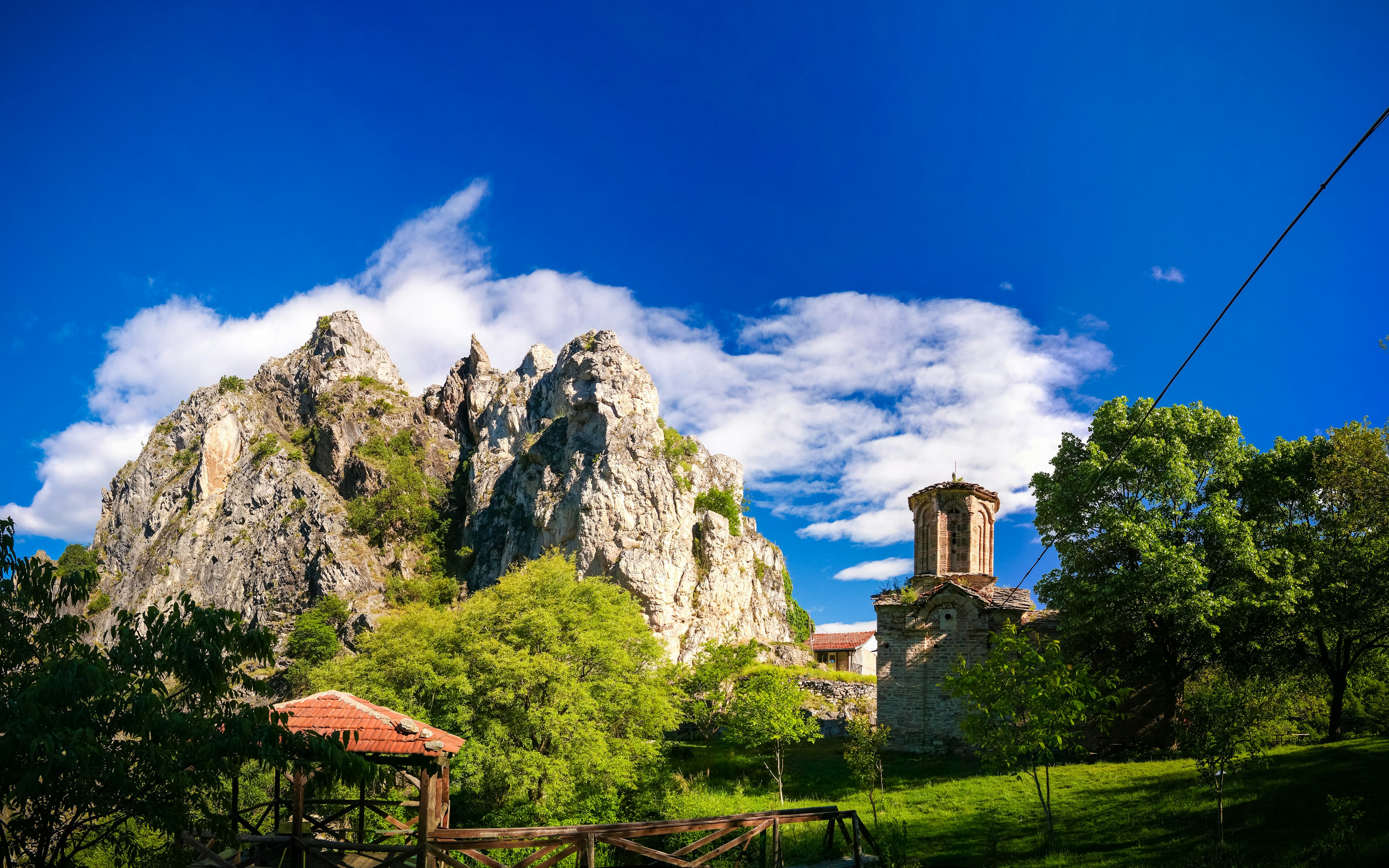 A stone monastery with red roofs is nestled between tall green trees and a portion of the jagged Sar mountain range; Best in Travel North Macedonia