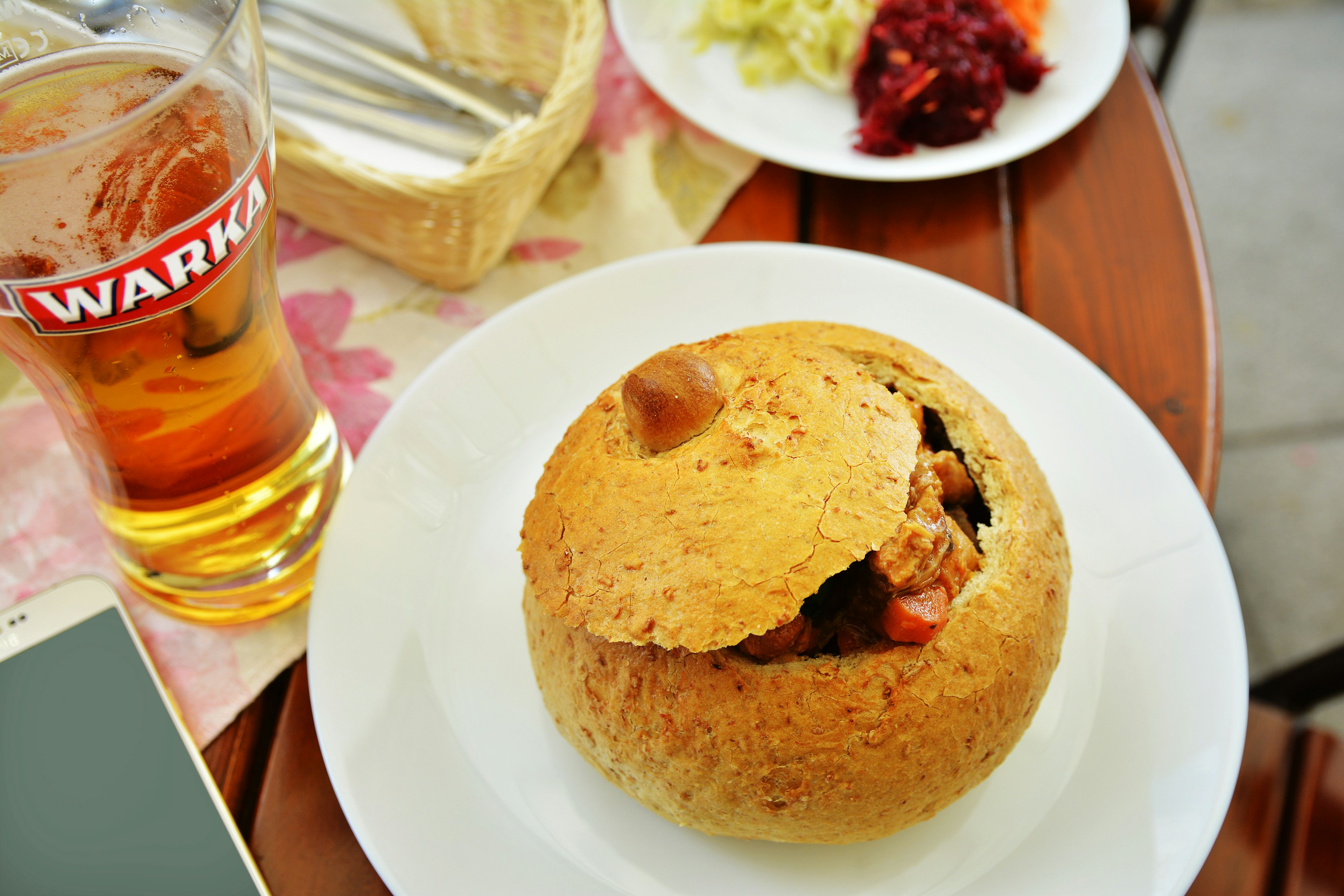 Pork goulash in bread and a beer sit on a table.