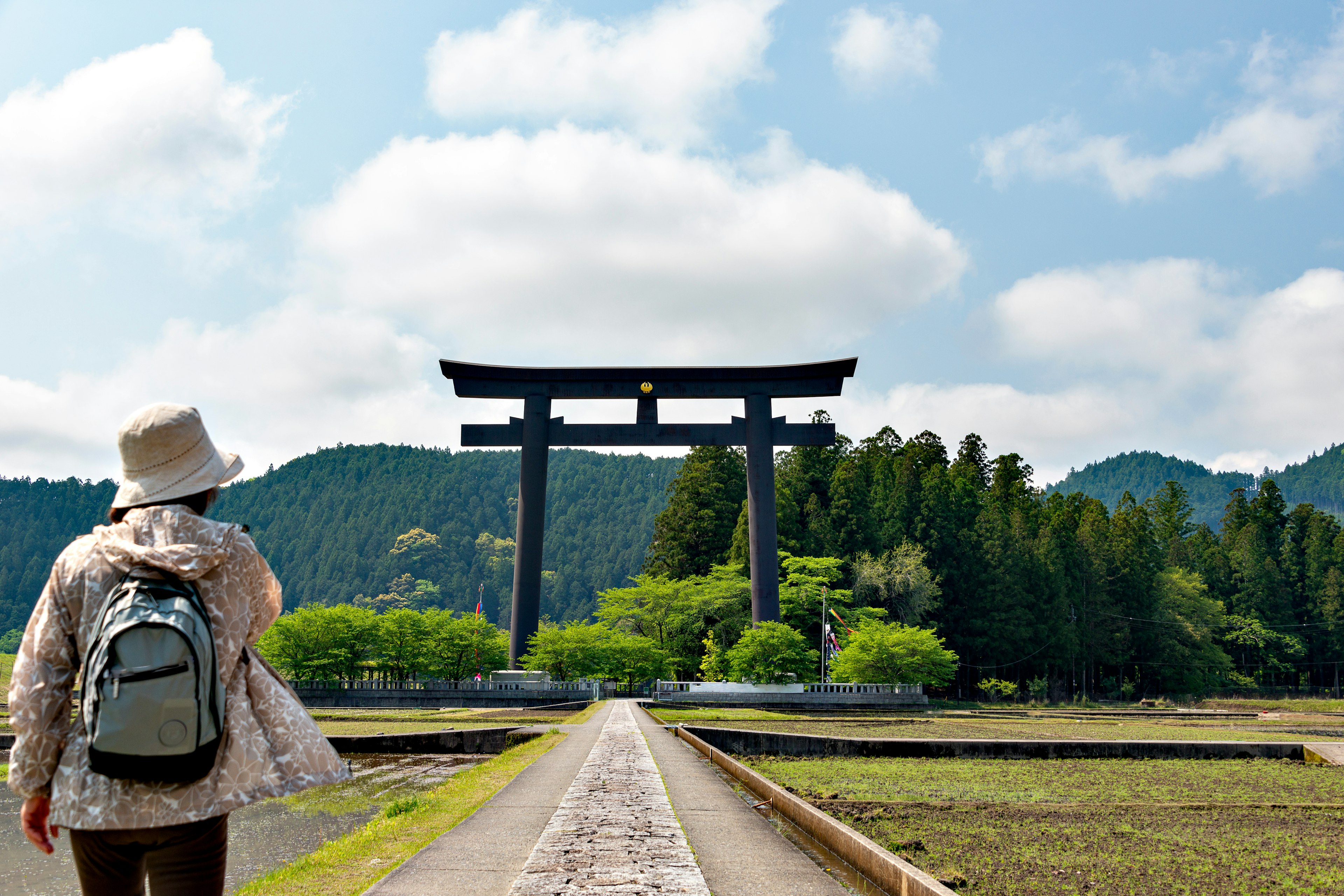 Woman stands in front of the large gateway to the Kumano Hongu Shrine.