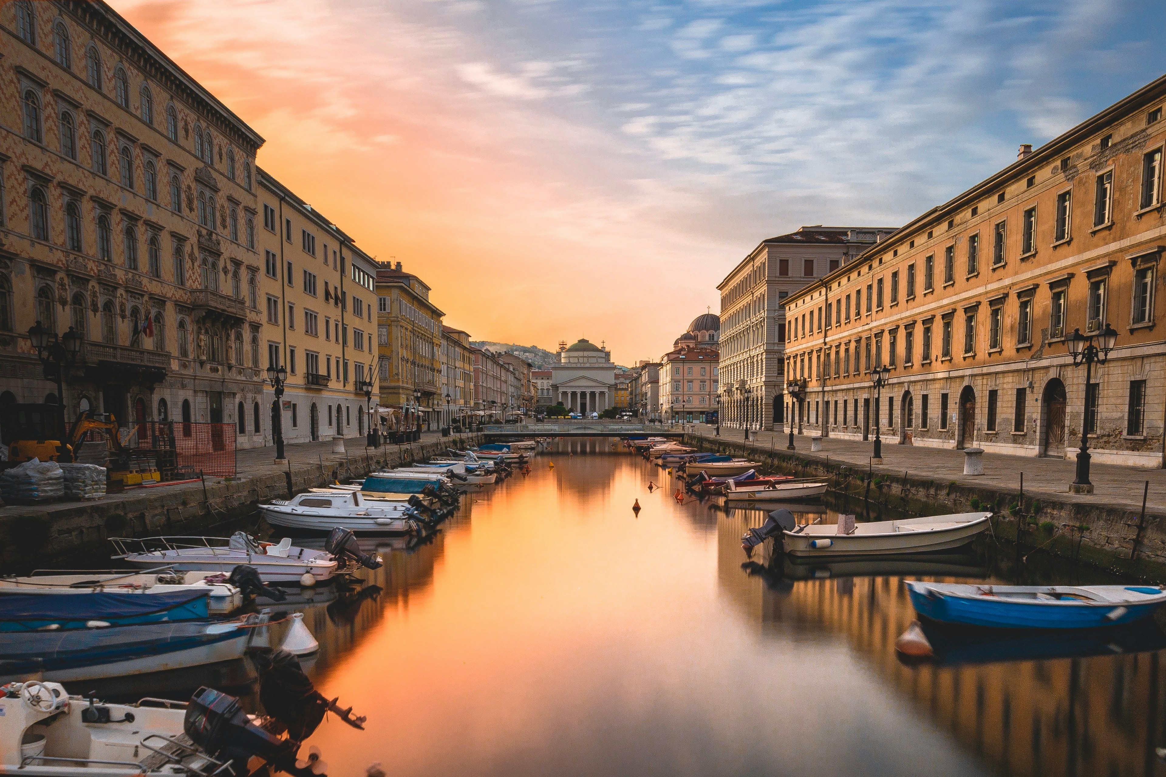 Looking down a canal at sunrise; there are boats on either side and it's lined with handsome palaces.