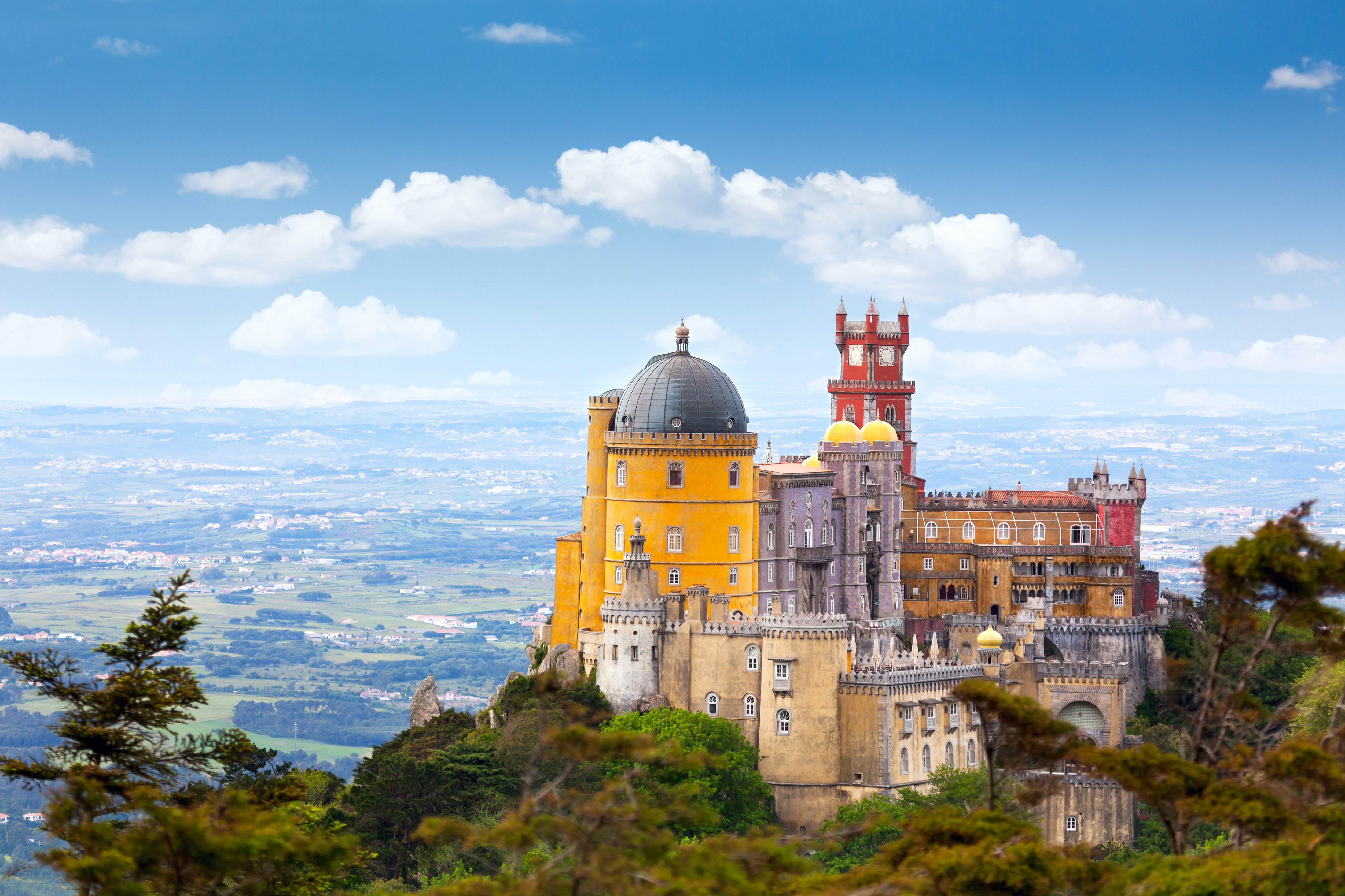 A castle complex on a hill in yellows and reds with domed turrets