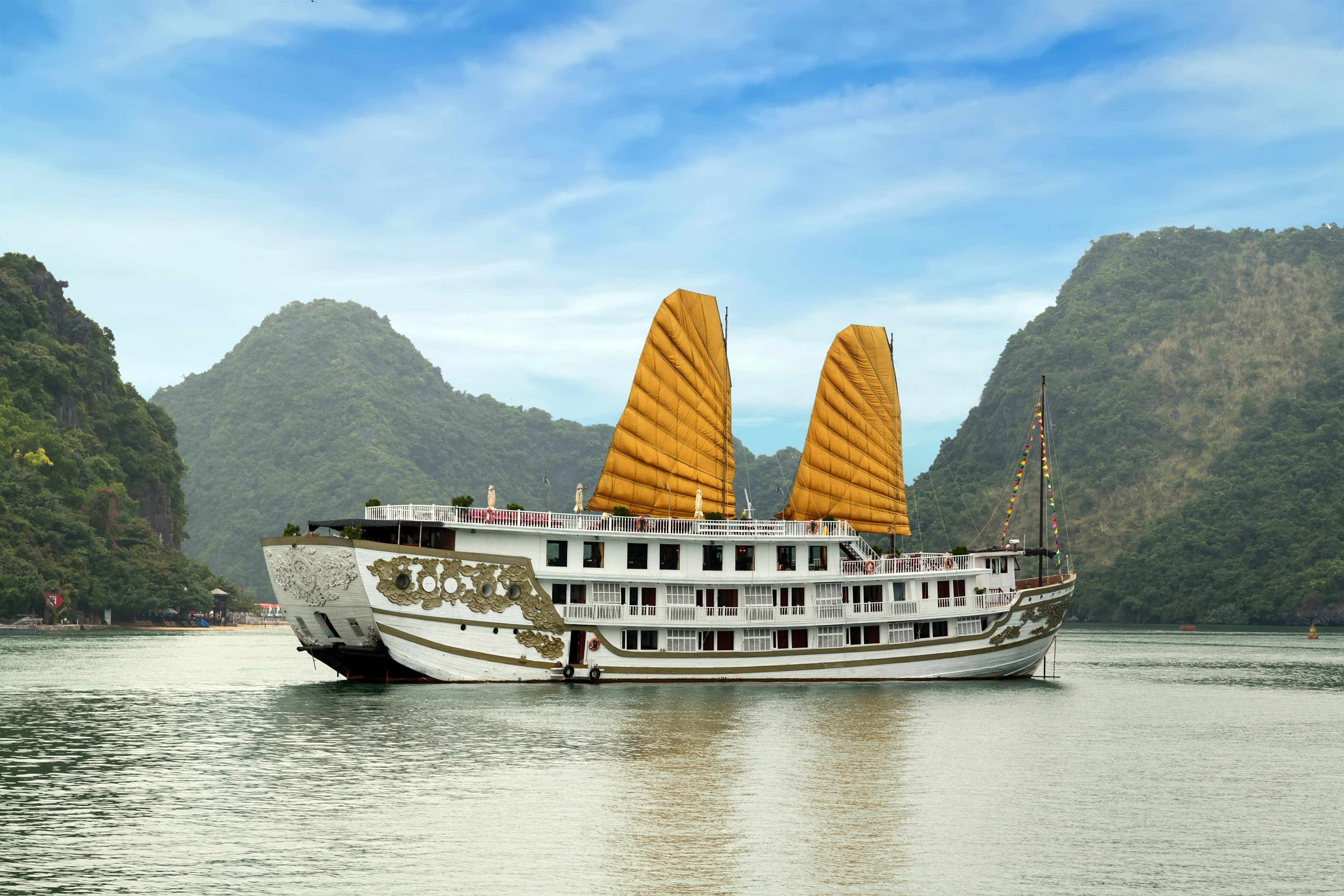 A cruise ship outfitted with a pair of large yellow sails glides along in Halong Bay