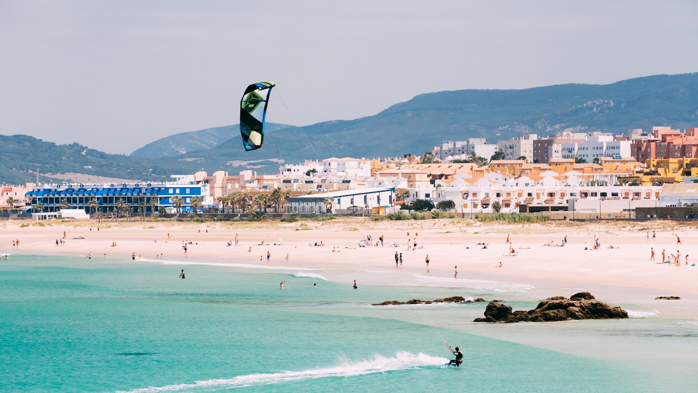 Kite surfing in Tarifa with beachgoers on the sand.