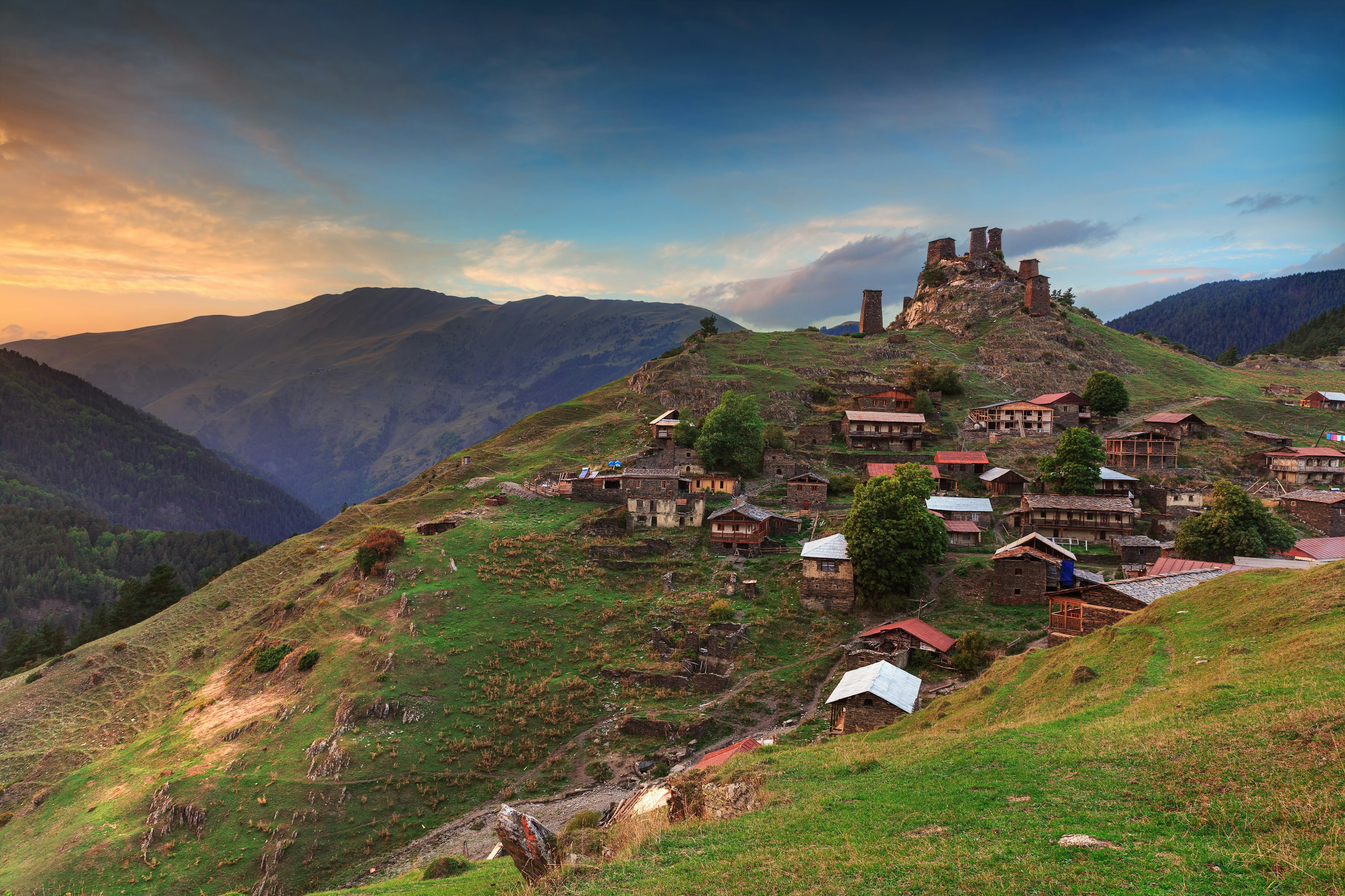 A remote village on a hilltop surrounded by hills and valleys. Several free-standing stone towers dominate the top of the hill.