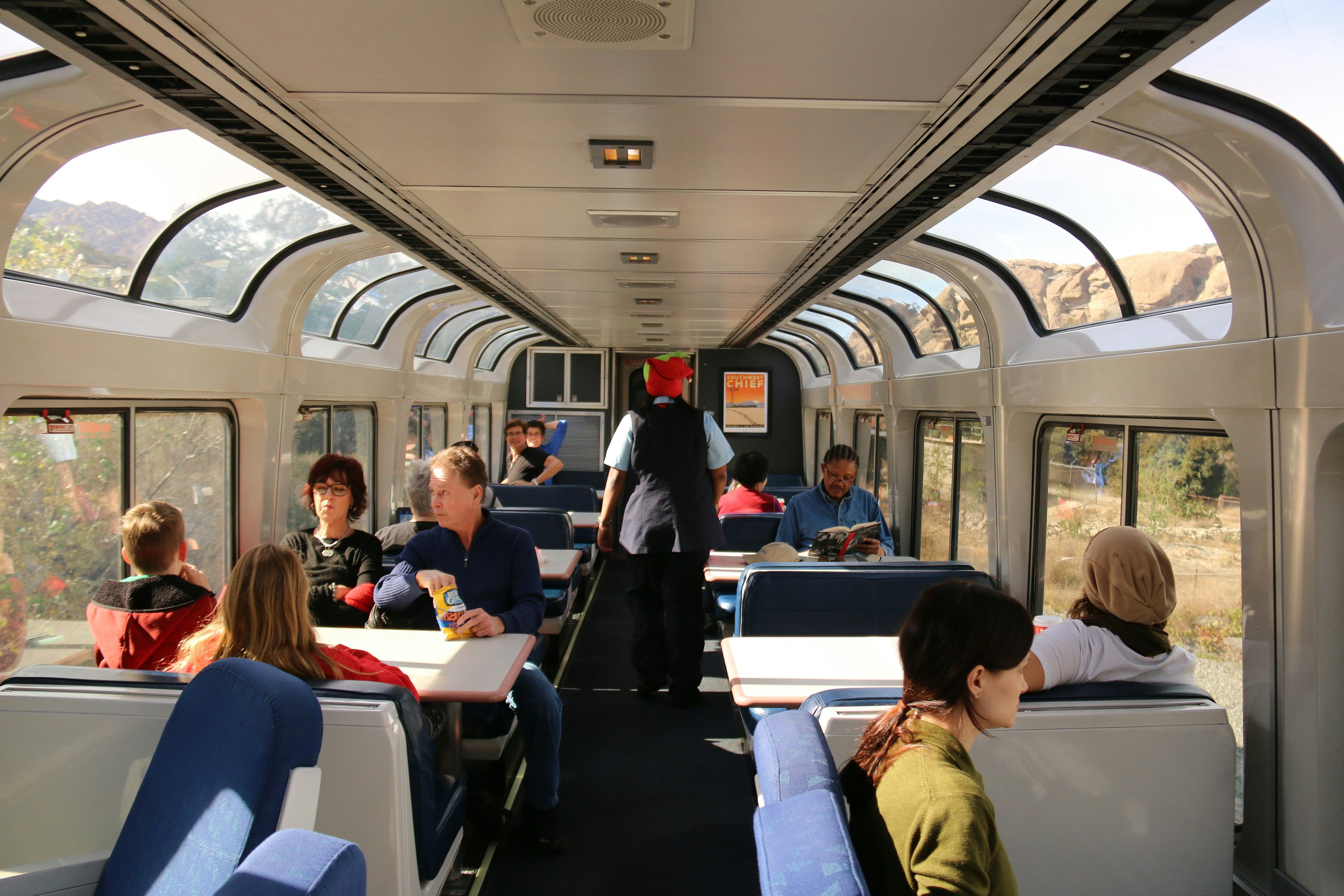 Passengers on an Amtrak lounge car with roomy tables and comfortable seating.