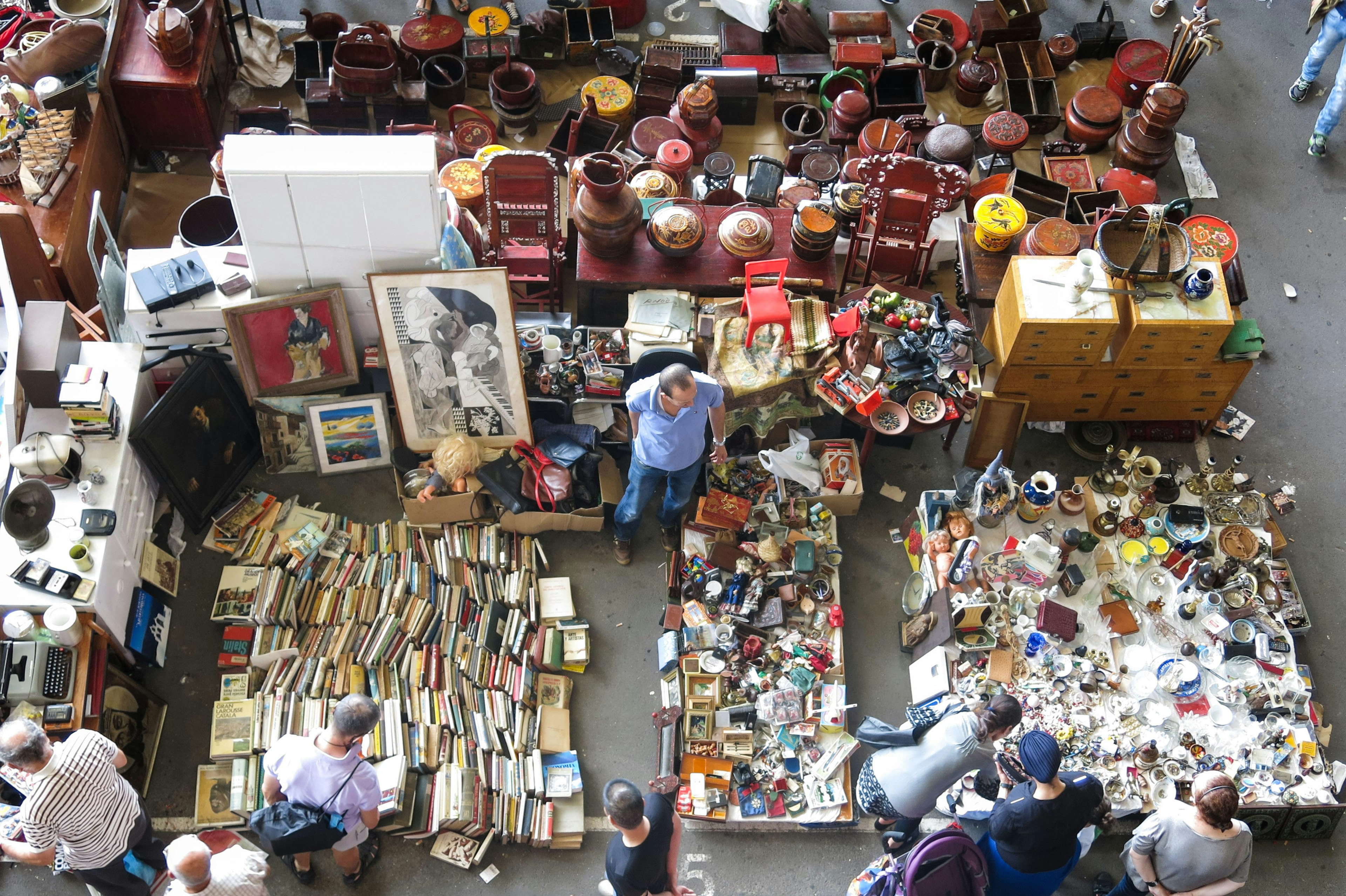 An overhead shot of tables, ledges and floor spaces completely covered in items for sale, including books, baskets, electronics, vases and trinkets.