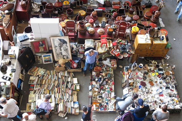 An overhead shot of tables, ledges and floor spaces completely covered in items for sale, including books, baskets, electronics, vases and trinkets.