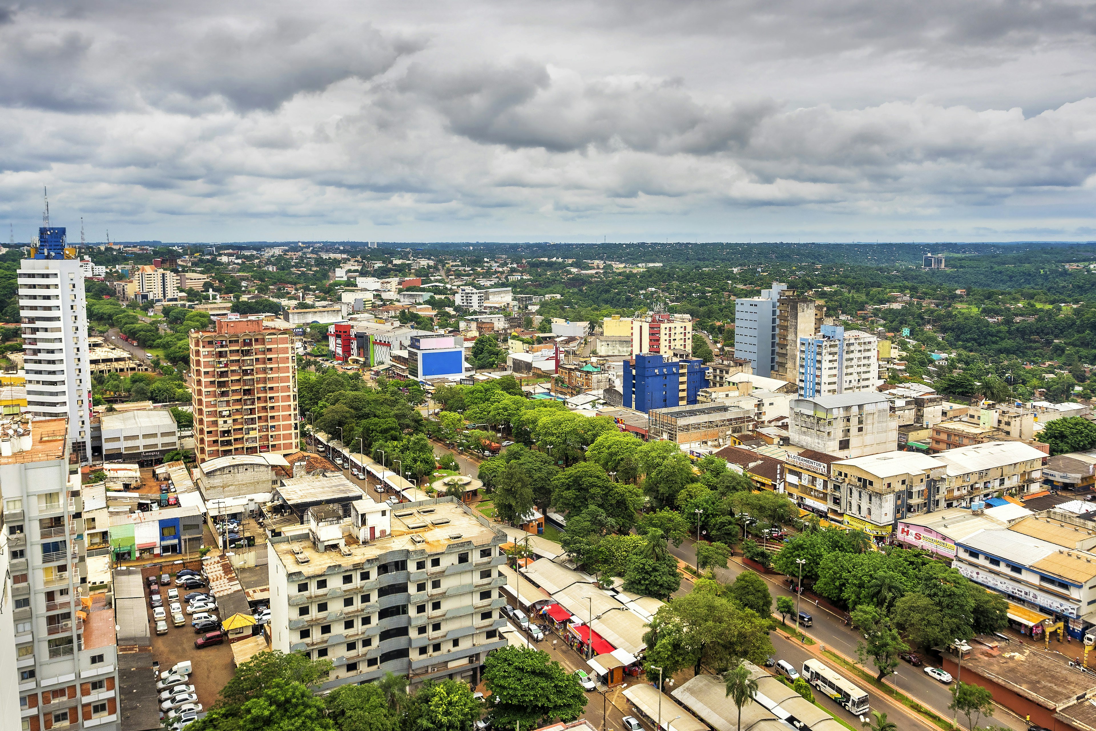 Aerial view of Ciudad del Este in Paraguay. Row of trees flank a downtown street and there are high-rise buildings dotted throughout the city.