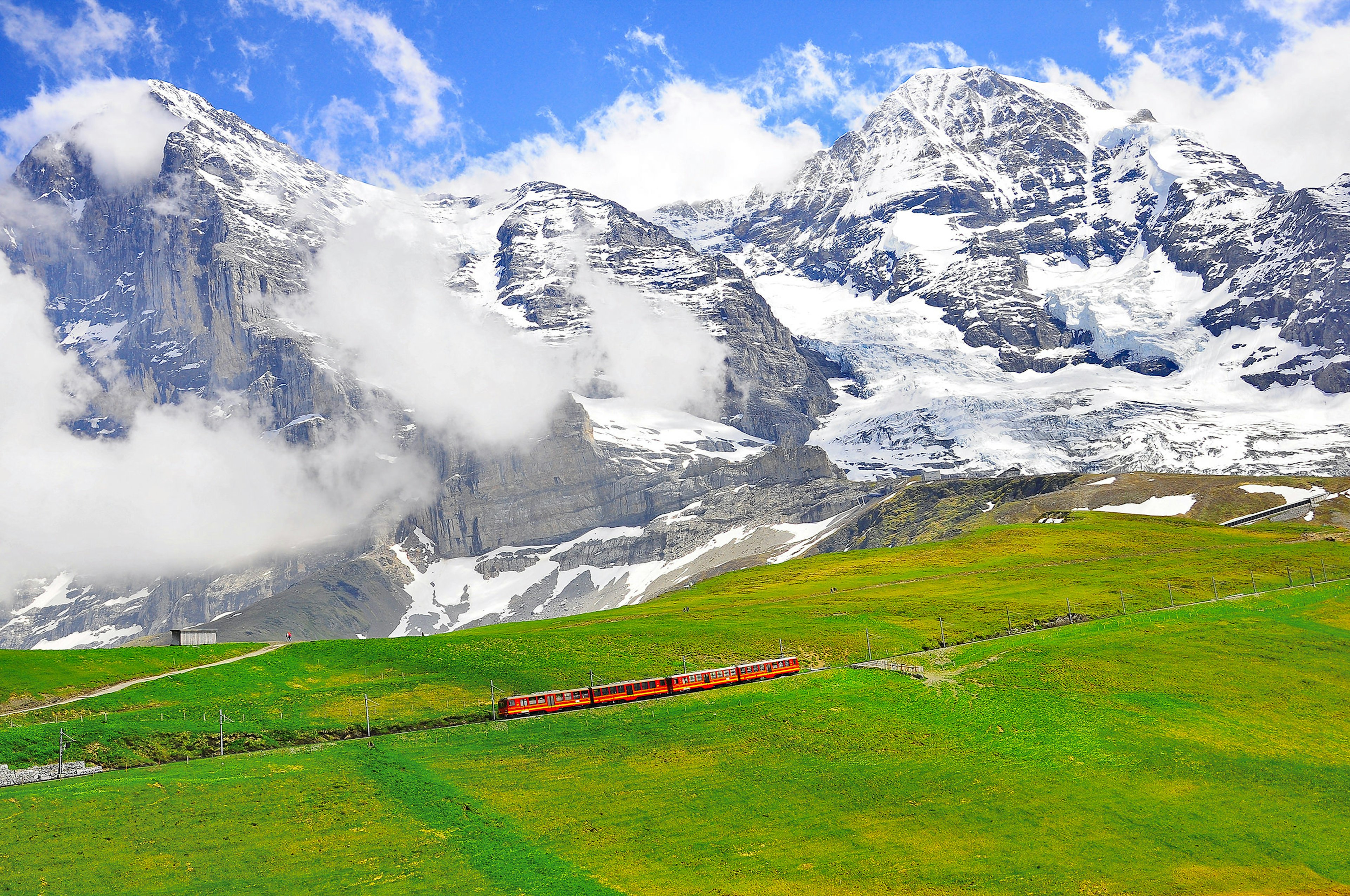 A four-carriage red train heads through a mountain landscape