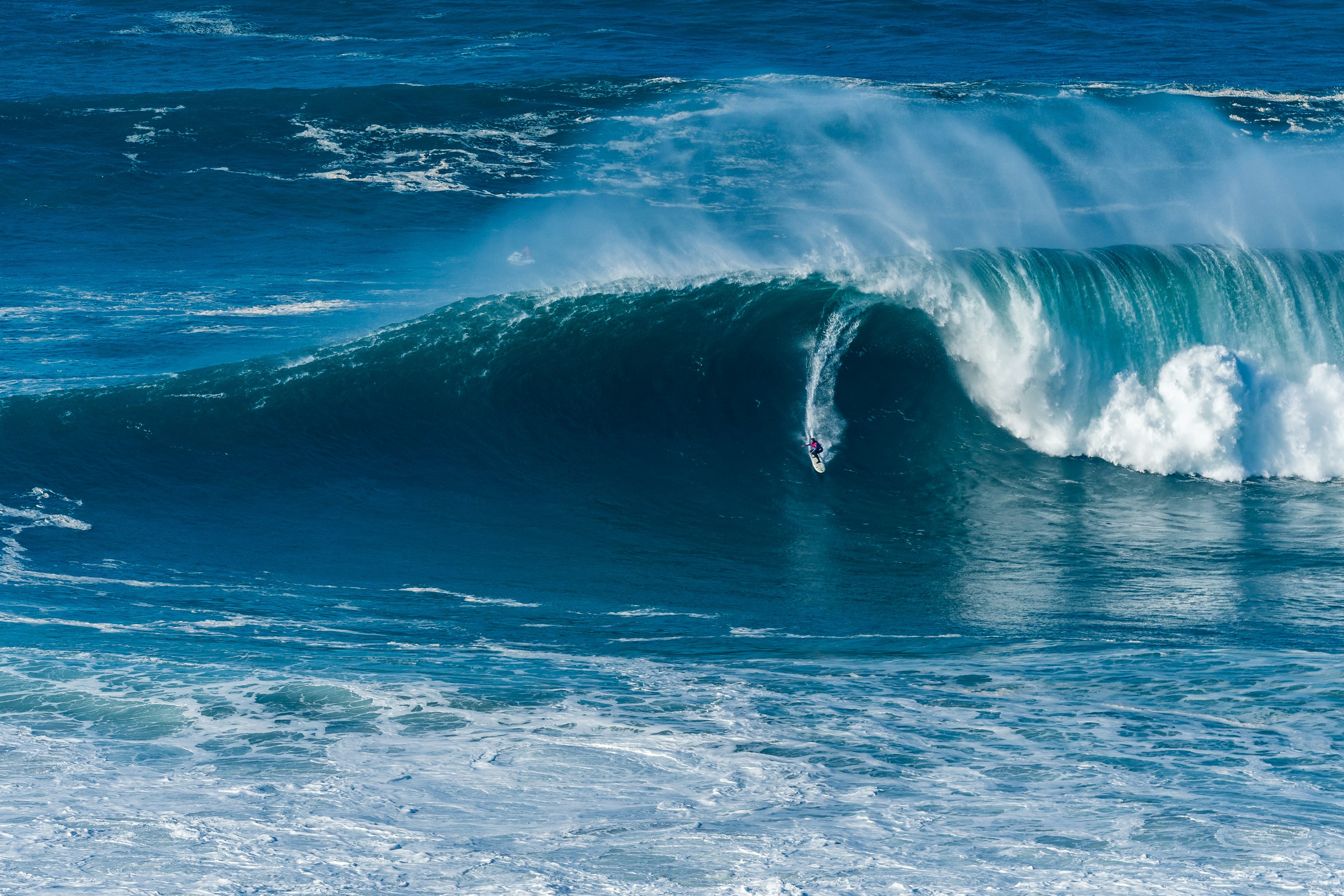 A surfer rides a huge wave crashing to one side of them and barelling to the other