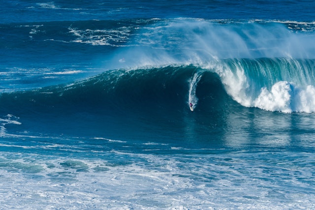 A surfer rides a huge wave crashing to one side of them and barelling to the other