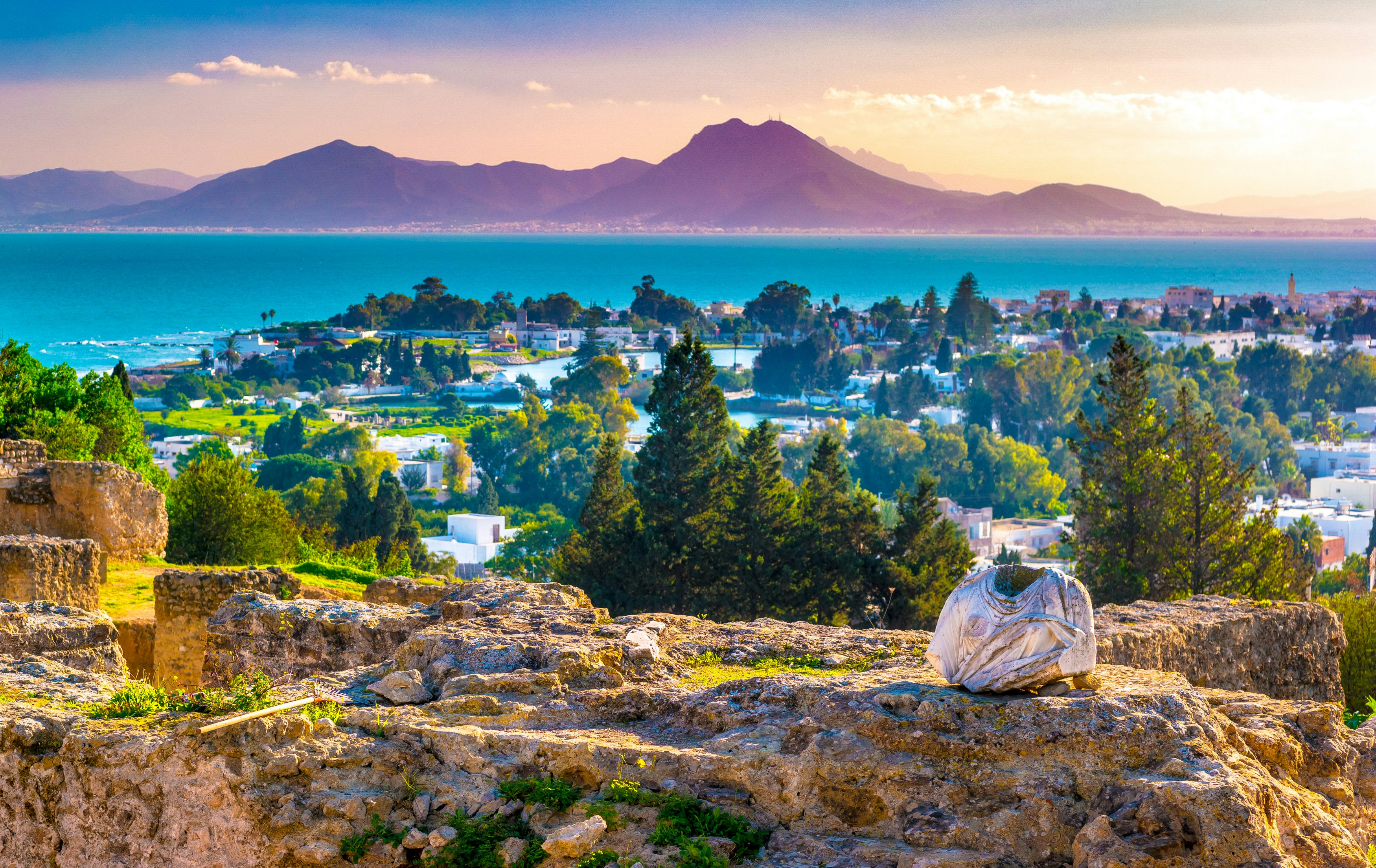 Ruins of the archaeological site of Byrsa Hill with the town of Carthage below; the whole scene overlooks the Mediterranean Sea, which is a vibrant shade of blue.