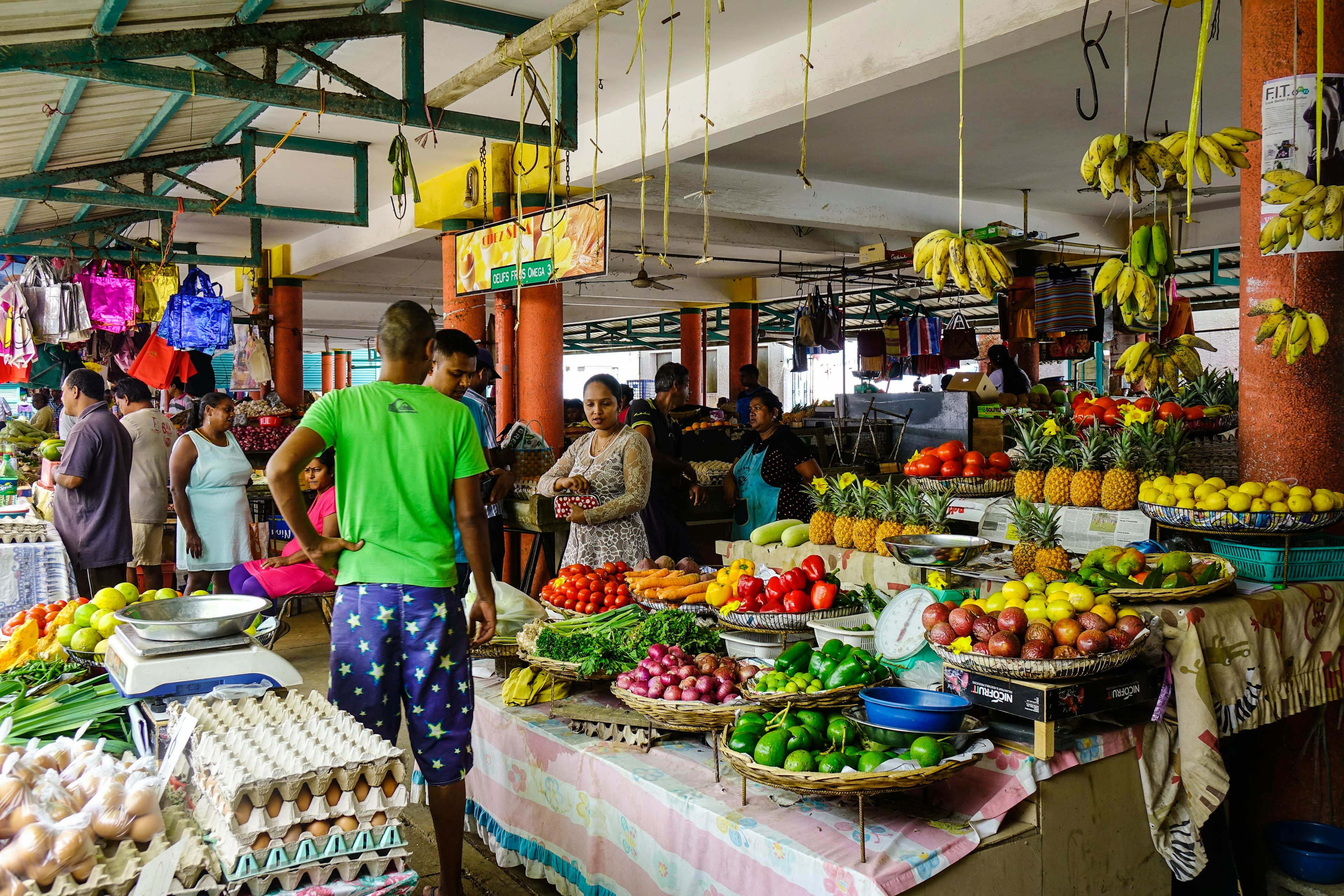 A Mauritius market, with people by a stall laden with colourful fresh produce.