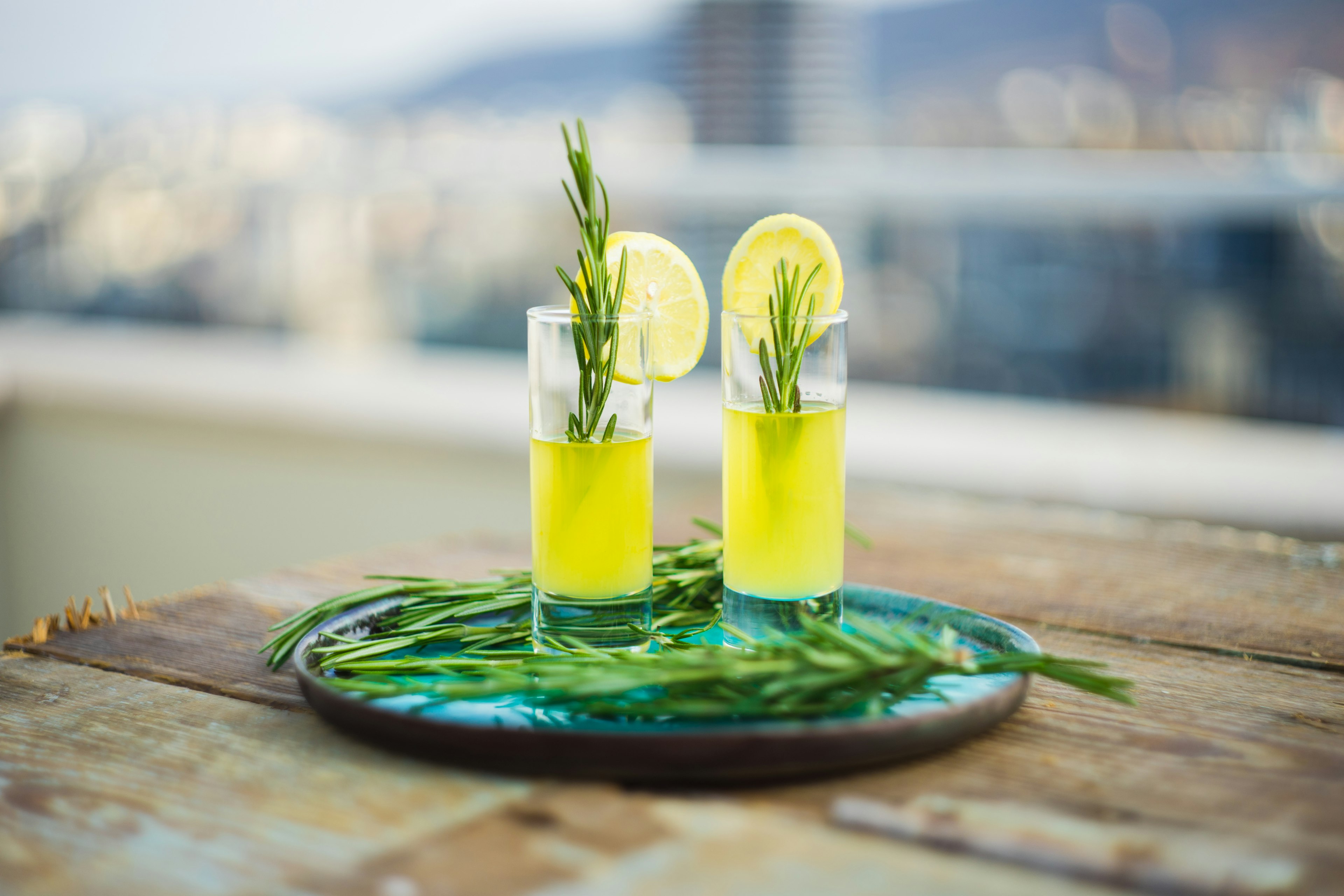 Traditional Italian lemon alcohol drink limoncello with pieces of lemon and rosemary herb on a dark wooden table.