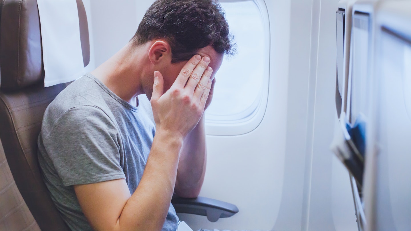 Man holding his head on the plane. Sunlight is coming through the window.