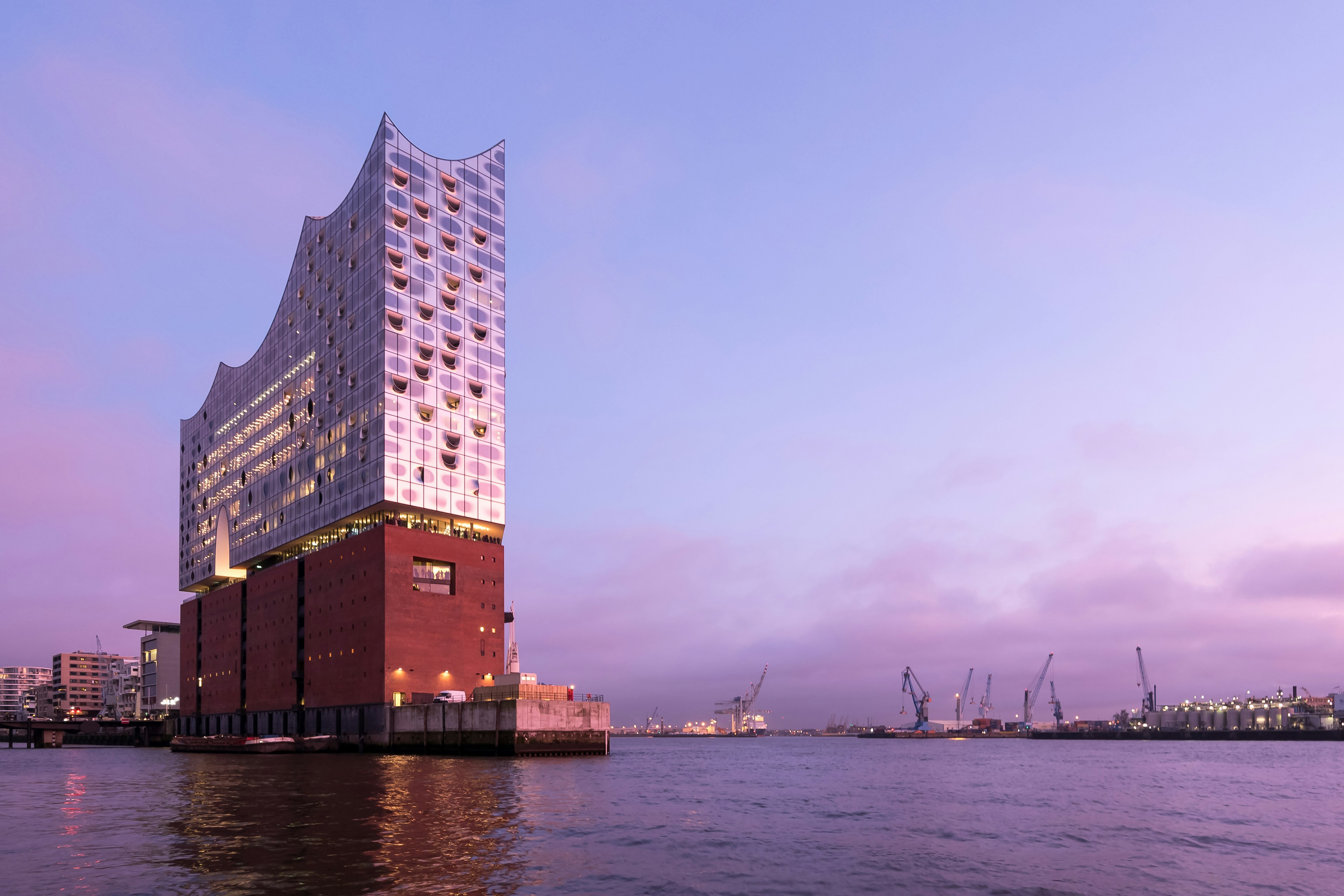 The Elbphilharmonie, viewed from the river, at dusk. A pink ligh is reflecting on the building's mirrored surface