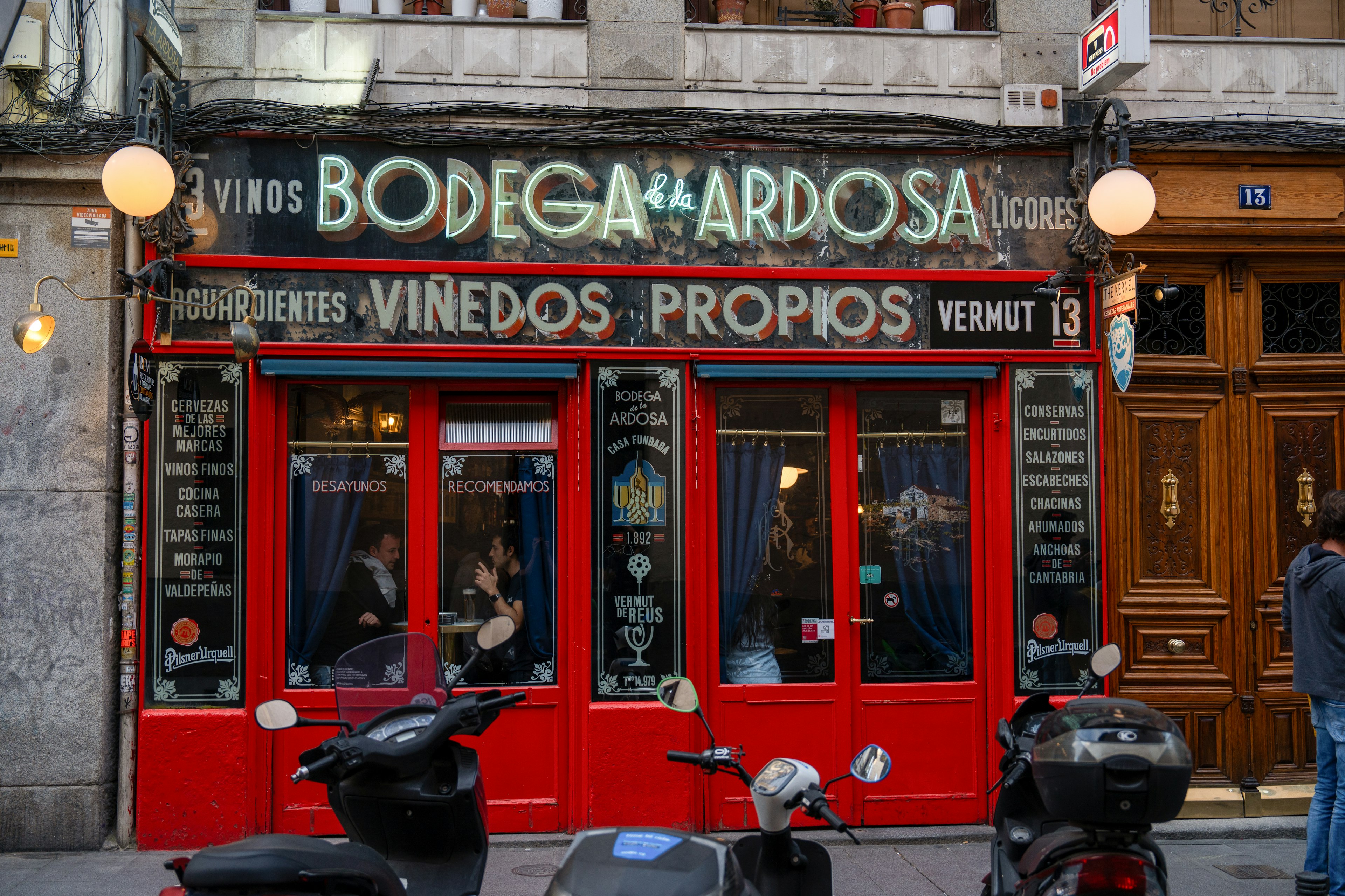 The bright red-painted facade of Bodega Ardosa, with old-fashioned signs announcing the bar's wares and mauve curtains hanging in the windows.