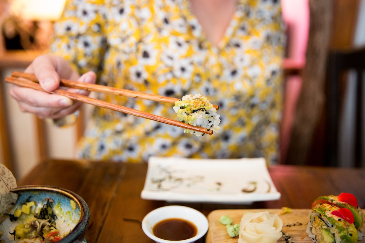 A person holding a sushi roll between chopsticks at Momo in Montréal, Canada