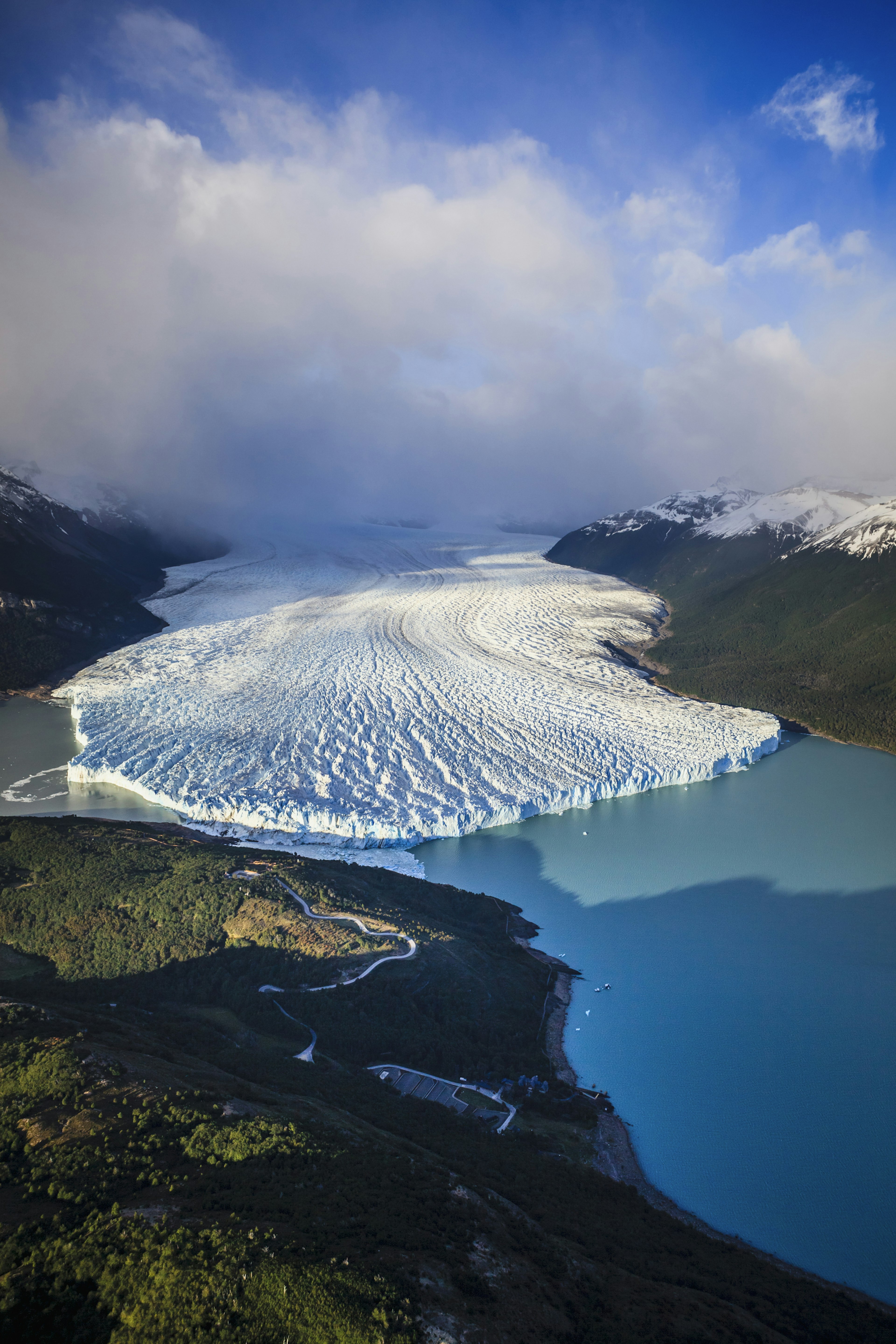 An aerial view of a glacial tongue extending into a sky-blue lake