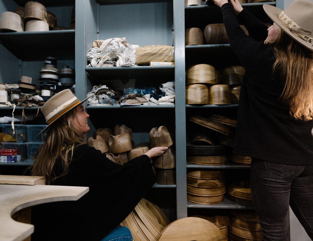 Two women shop stand by shelves filled with materials for making hats