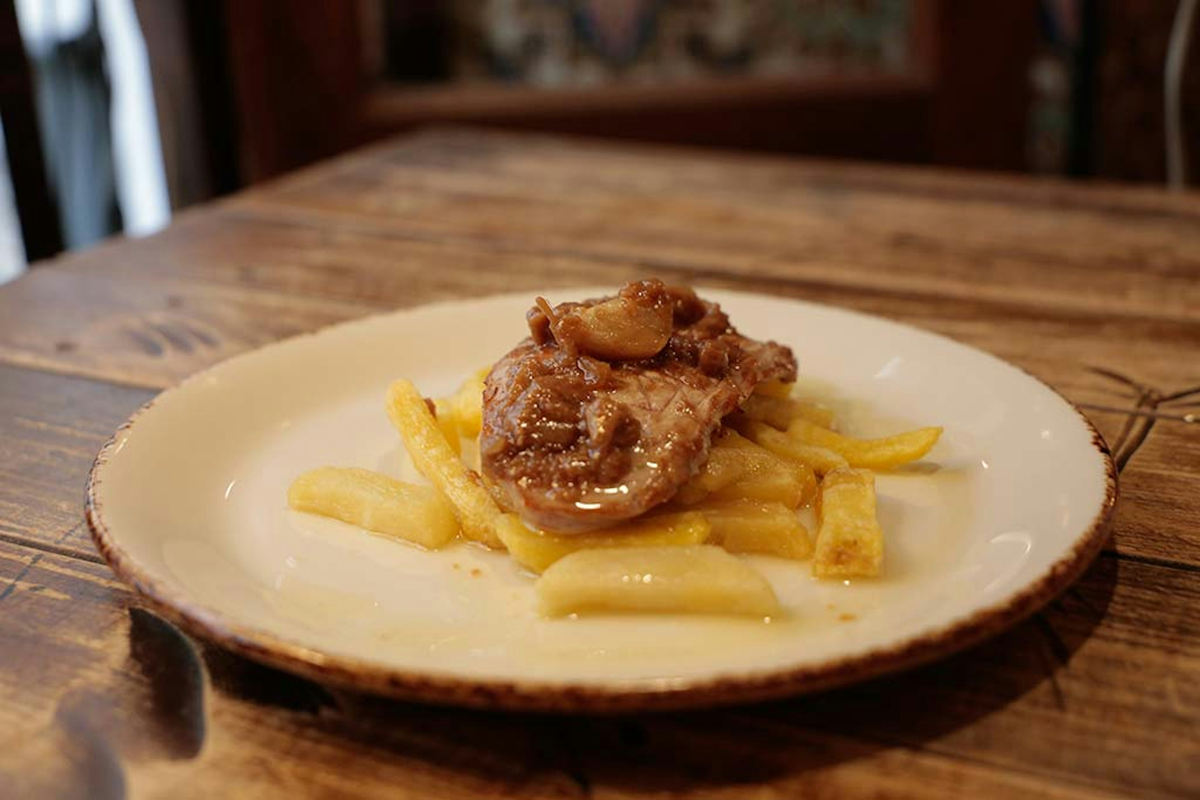 A small plate of pork with fries on a wooden table