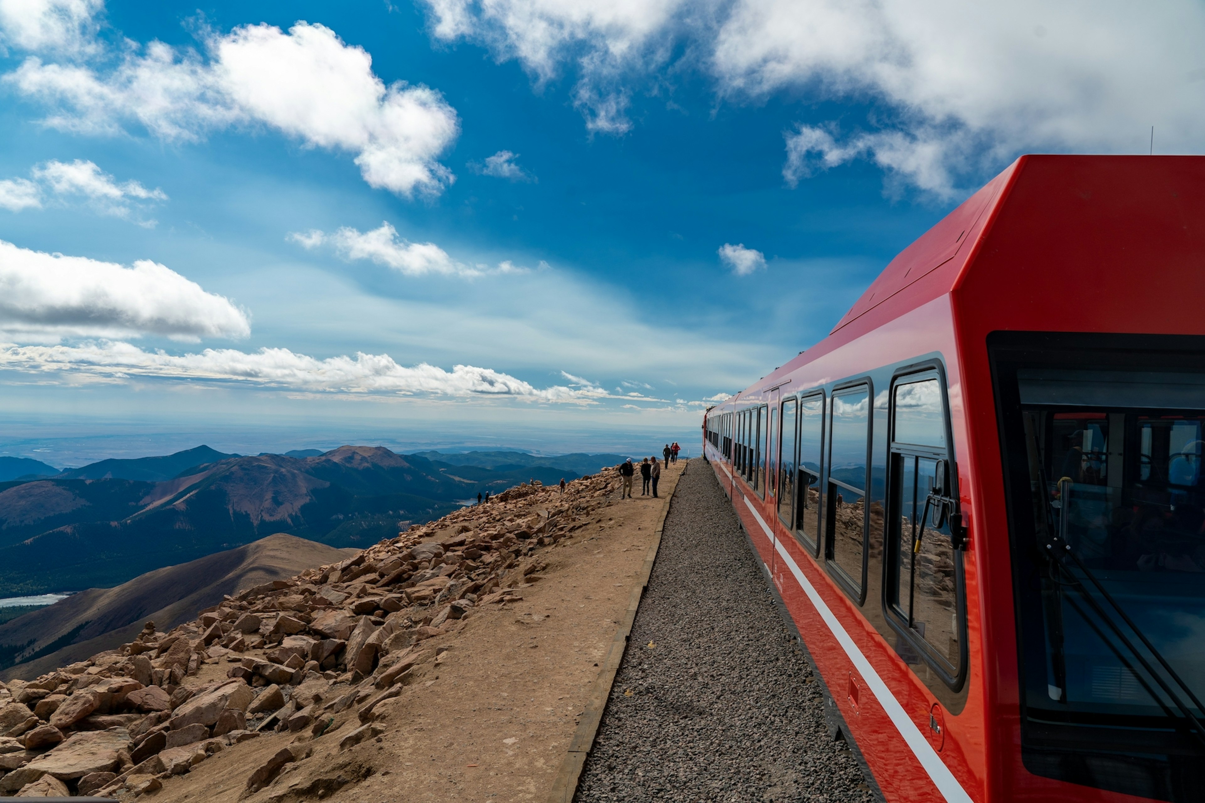 A view of a the red cards of a Pikes Peak Cog Railway train waiting to load passengers for their return trip to the lower station, with a vista of mountains in the distance, Colorado, USA