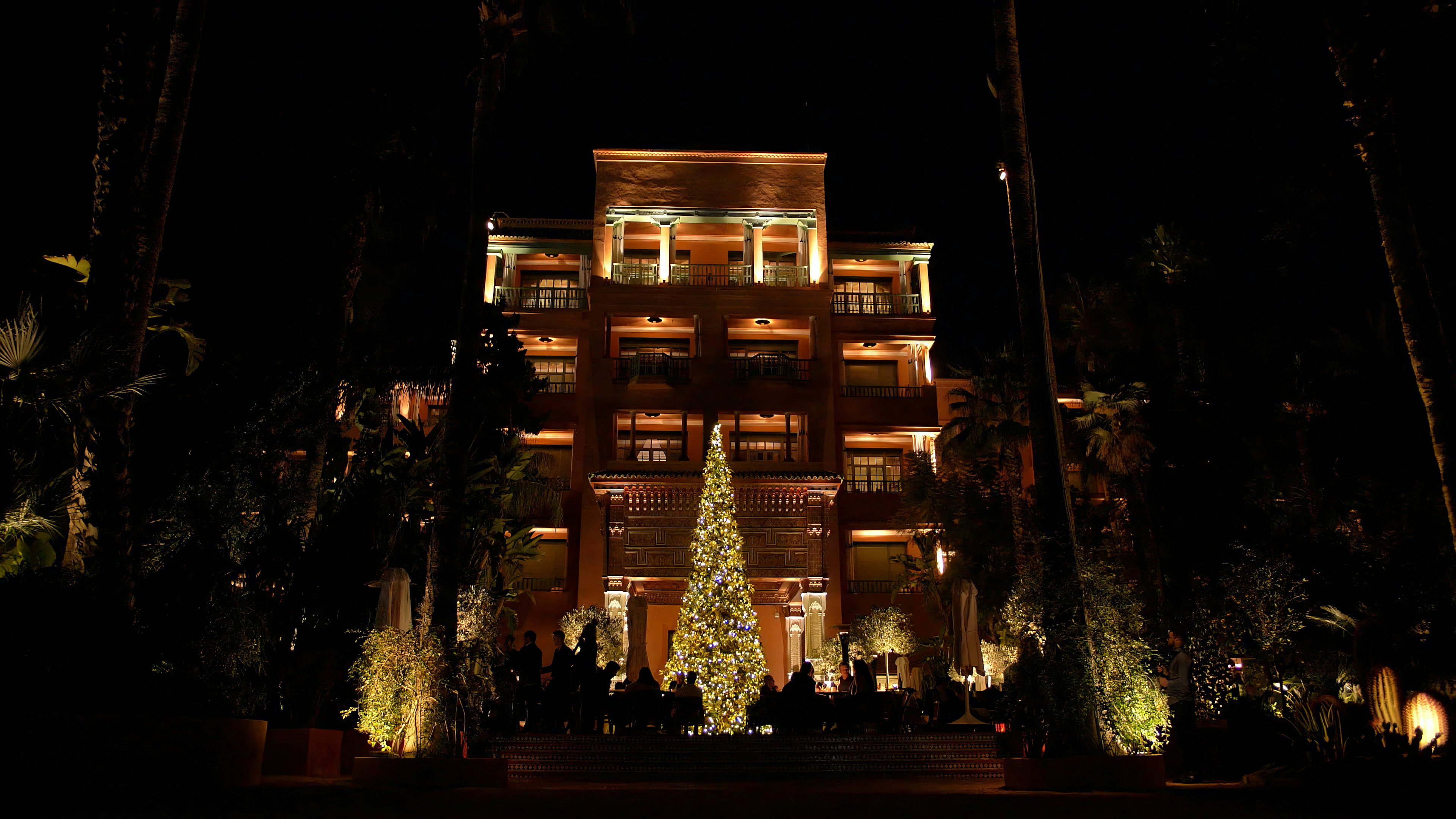 A low-lit hotel with a large Christmas tree alight at the front