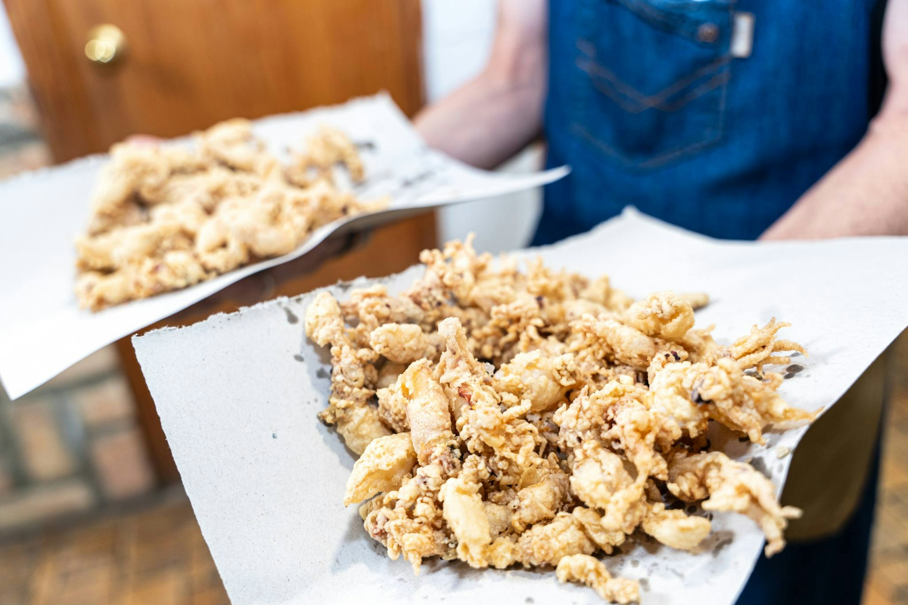 A member of waiting staff carries two small plates loaded with battered fried fish