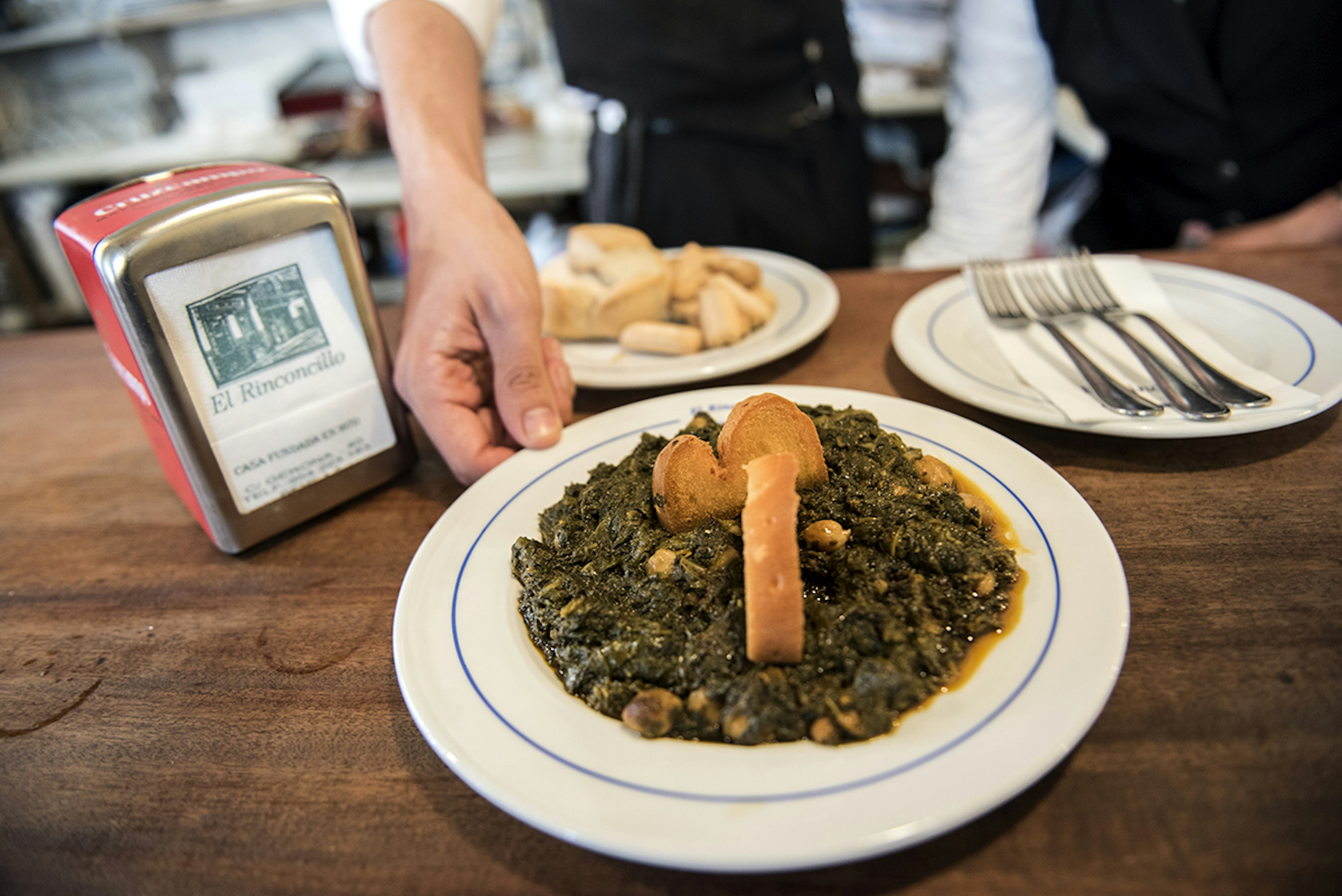 A member of staff places a dish of spinach with chickpeas on a table