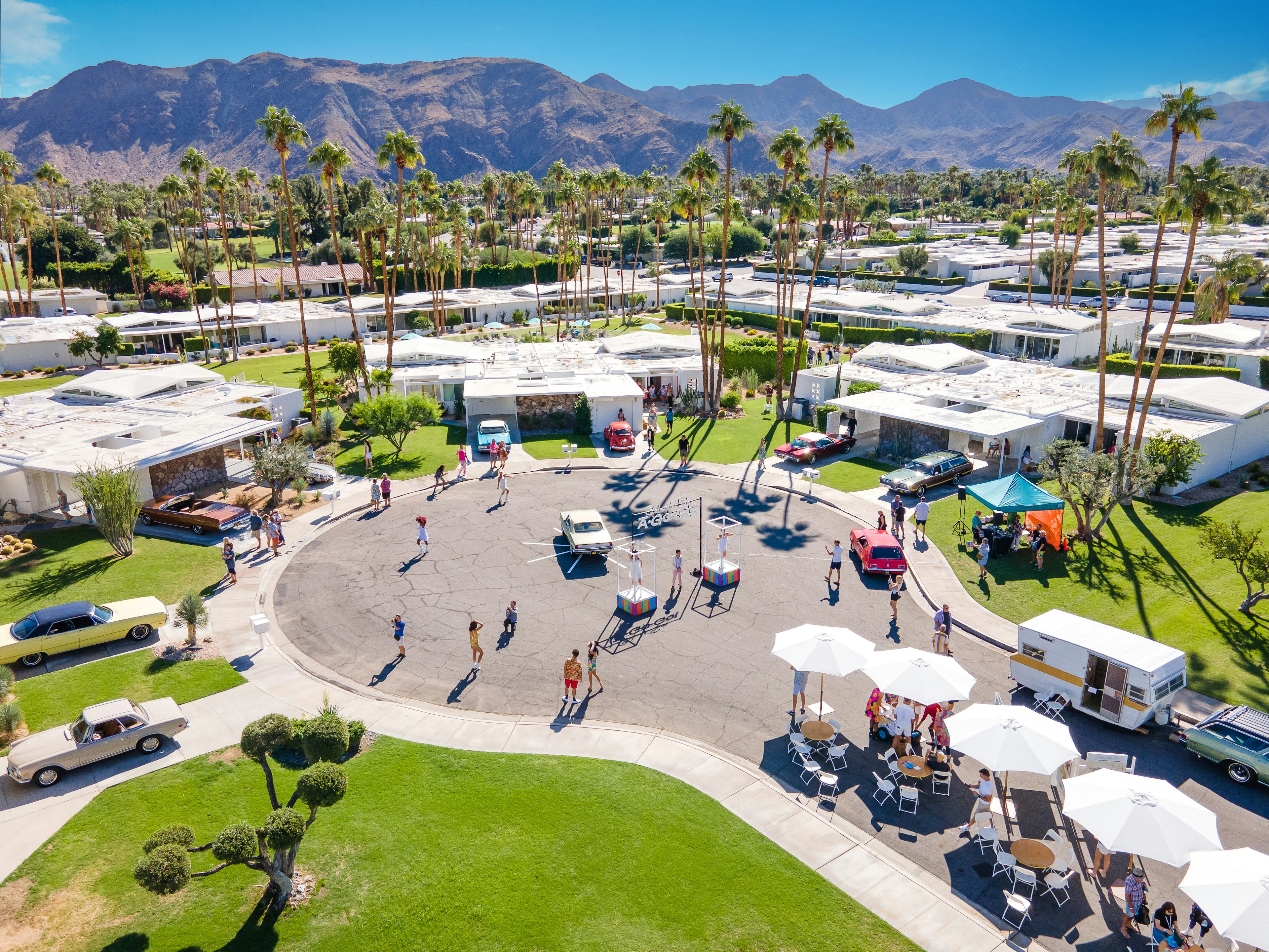 In an overhead shot, booths and vendors are seen set up in a cul-de-sac with several examples of modernist architecture and classic cars.