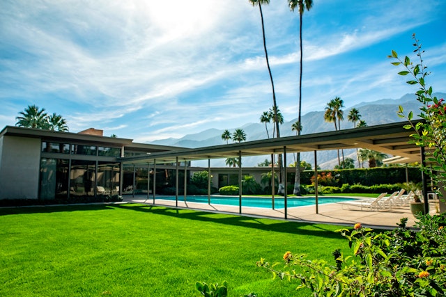 The modernist exterior of Frank Sinatra's home in Greater Palm Springs. Two tall trees rise above a pool shaped like a piano.