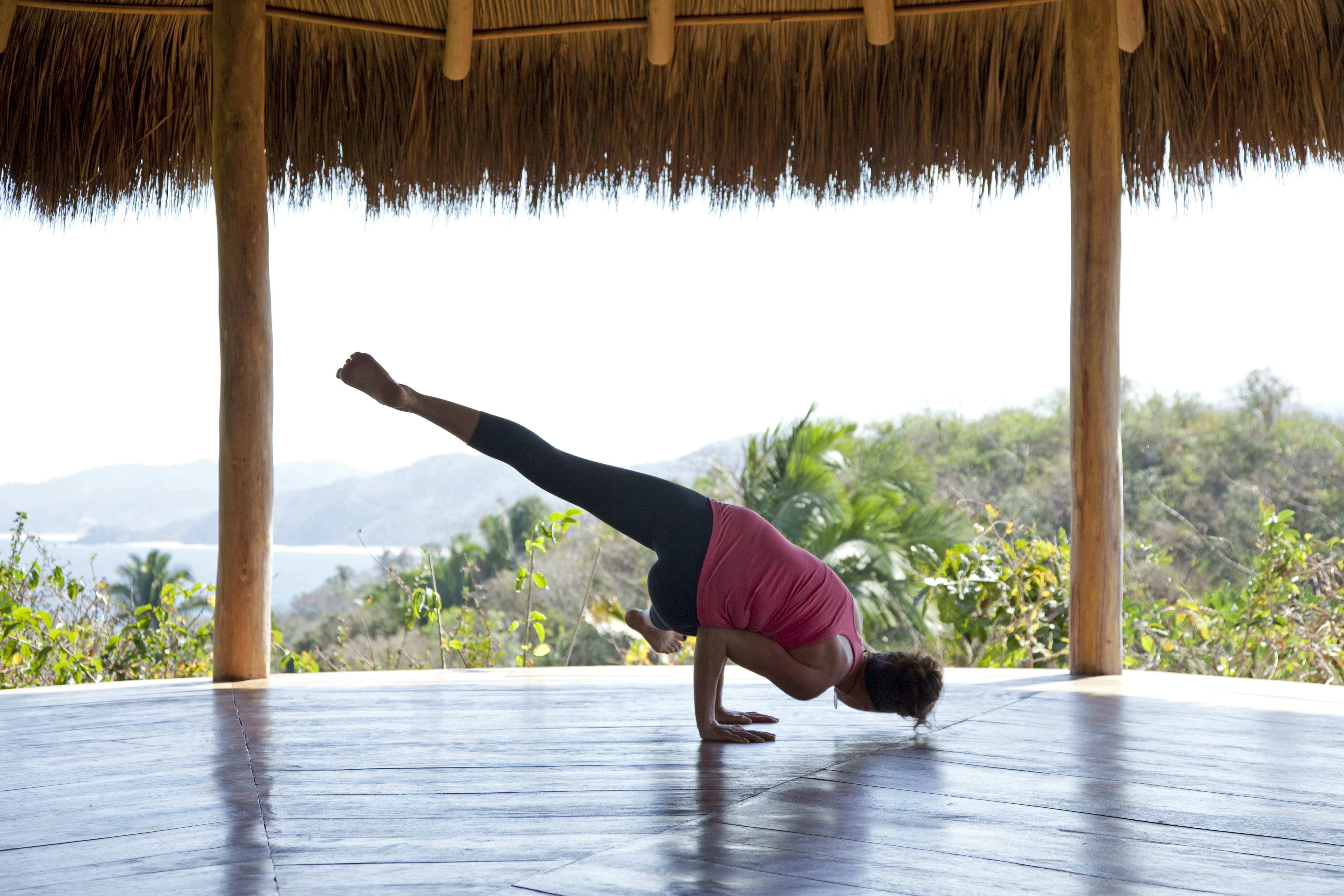 A woman practicing yoga in a pavilion overlooking hills and the ocean