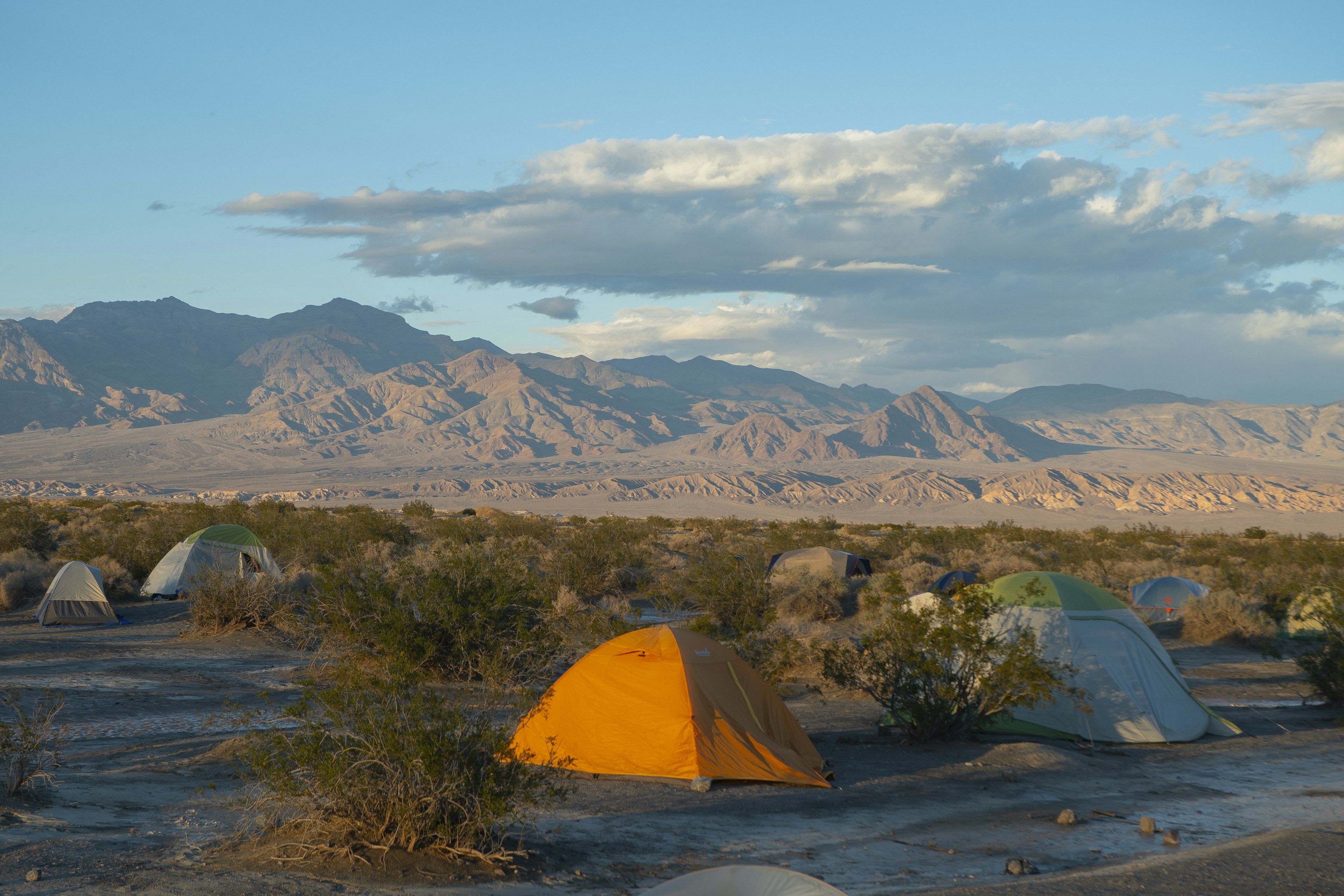 A group of tents set up on a plateau surrounded by mountain peaks in an arid national park