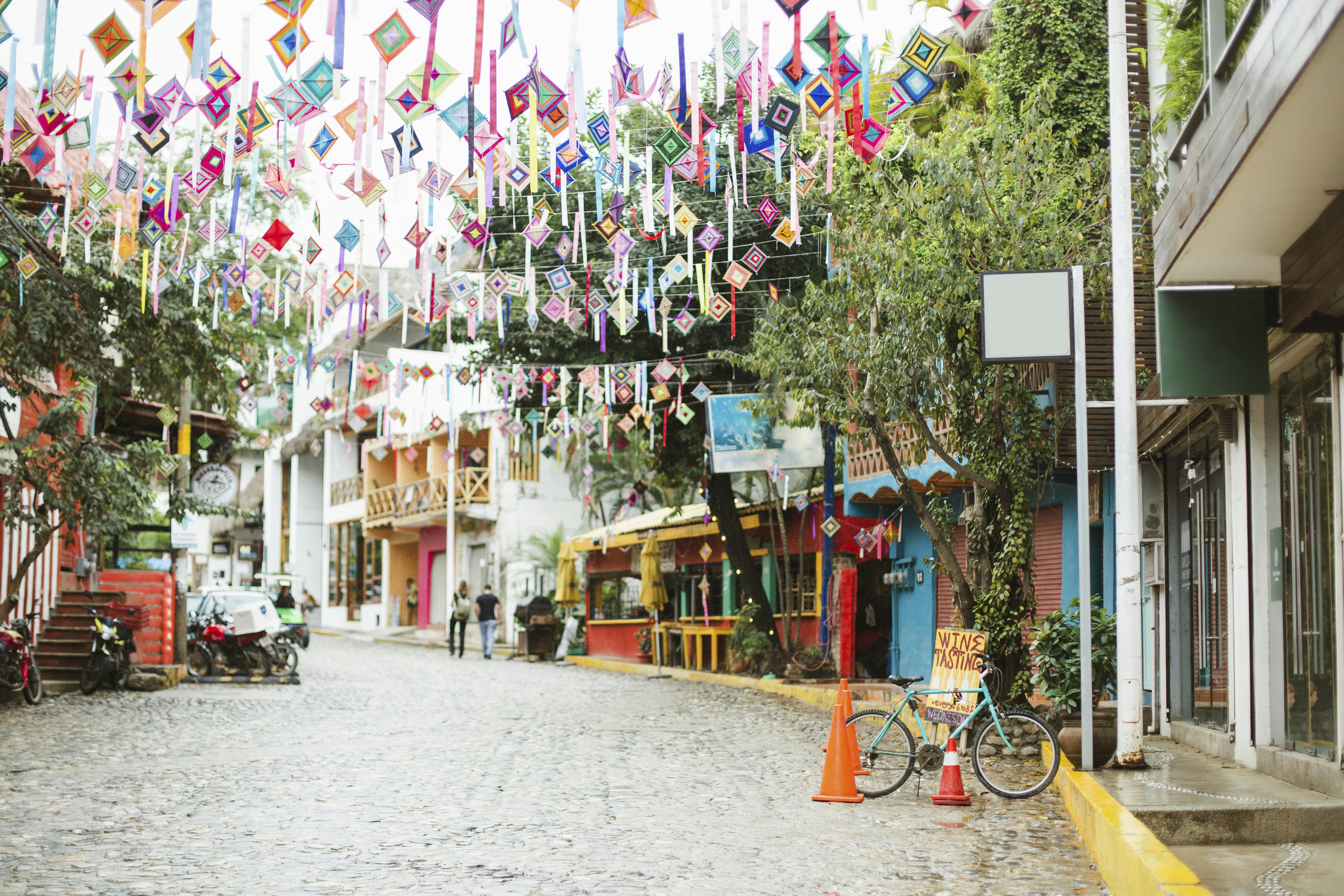 A cobbled street lined with colorfully painted shops, with flags and decorations strewn above