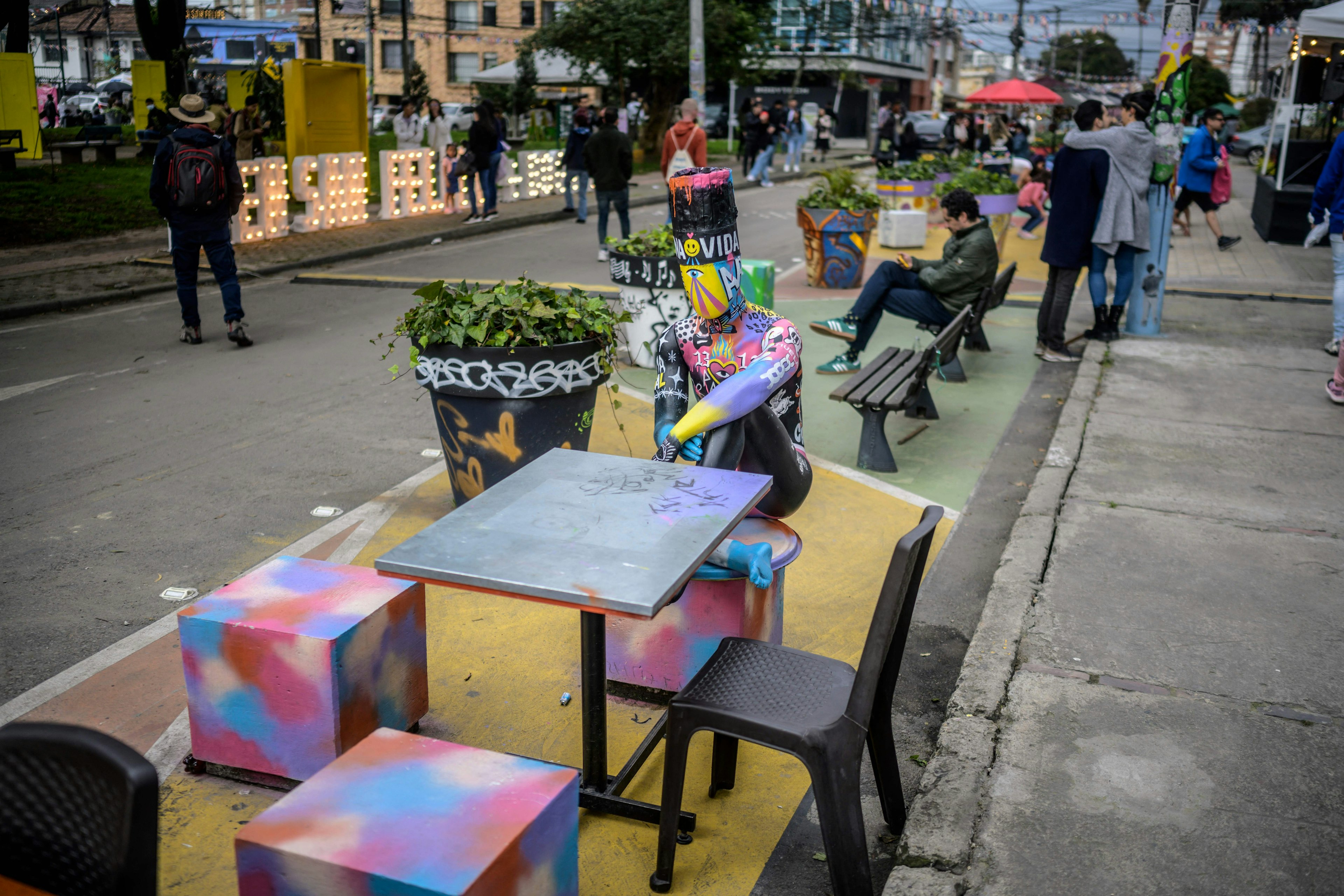 People pass by a street decorated with painted stools and tables for the Open San Felipe festival in Bogota, Colombia