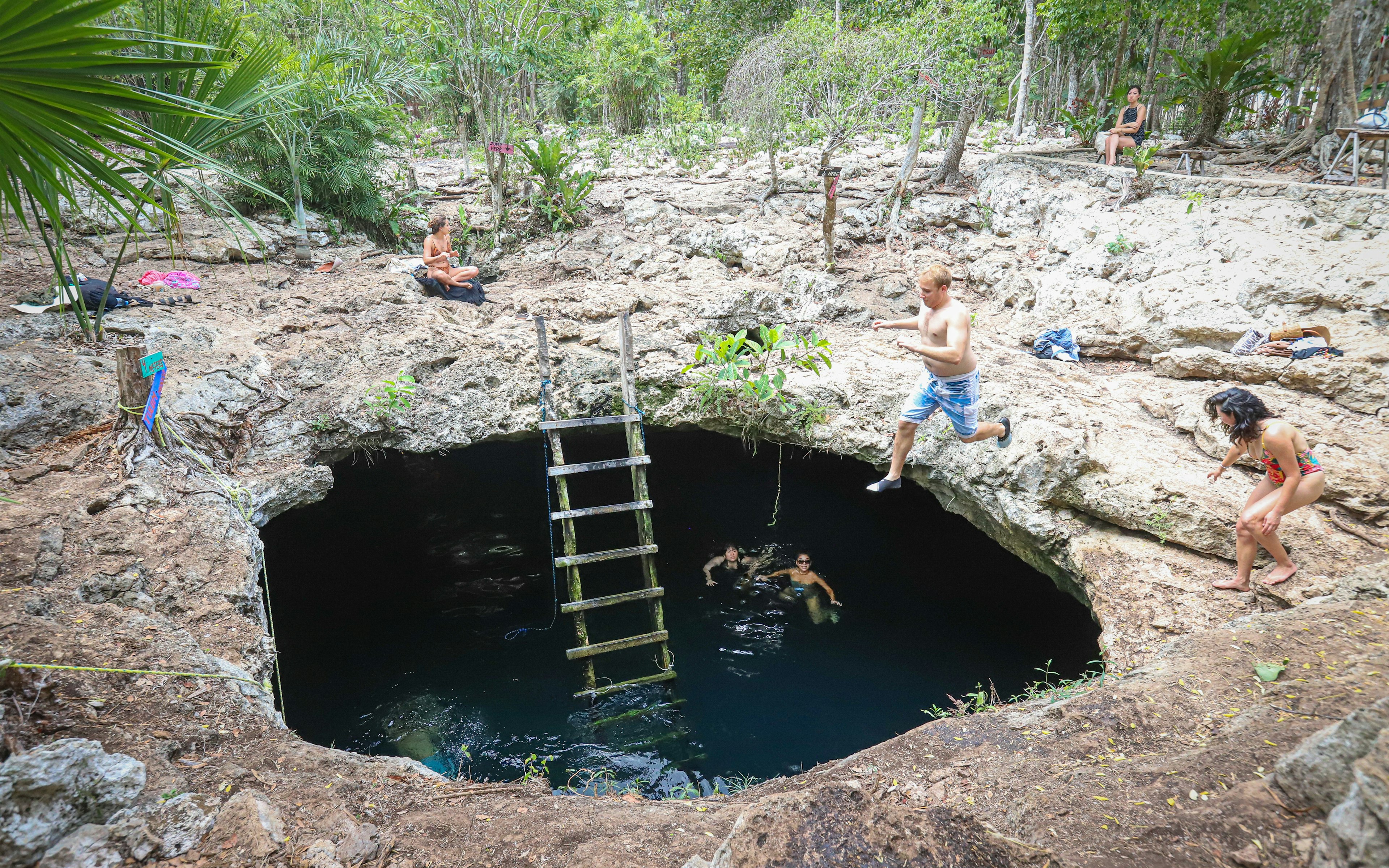 A man jumps off a rocky ledge through a hole to swim in the cave below.