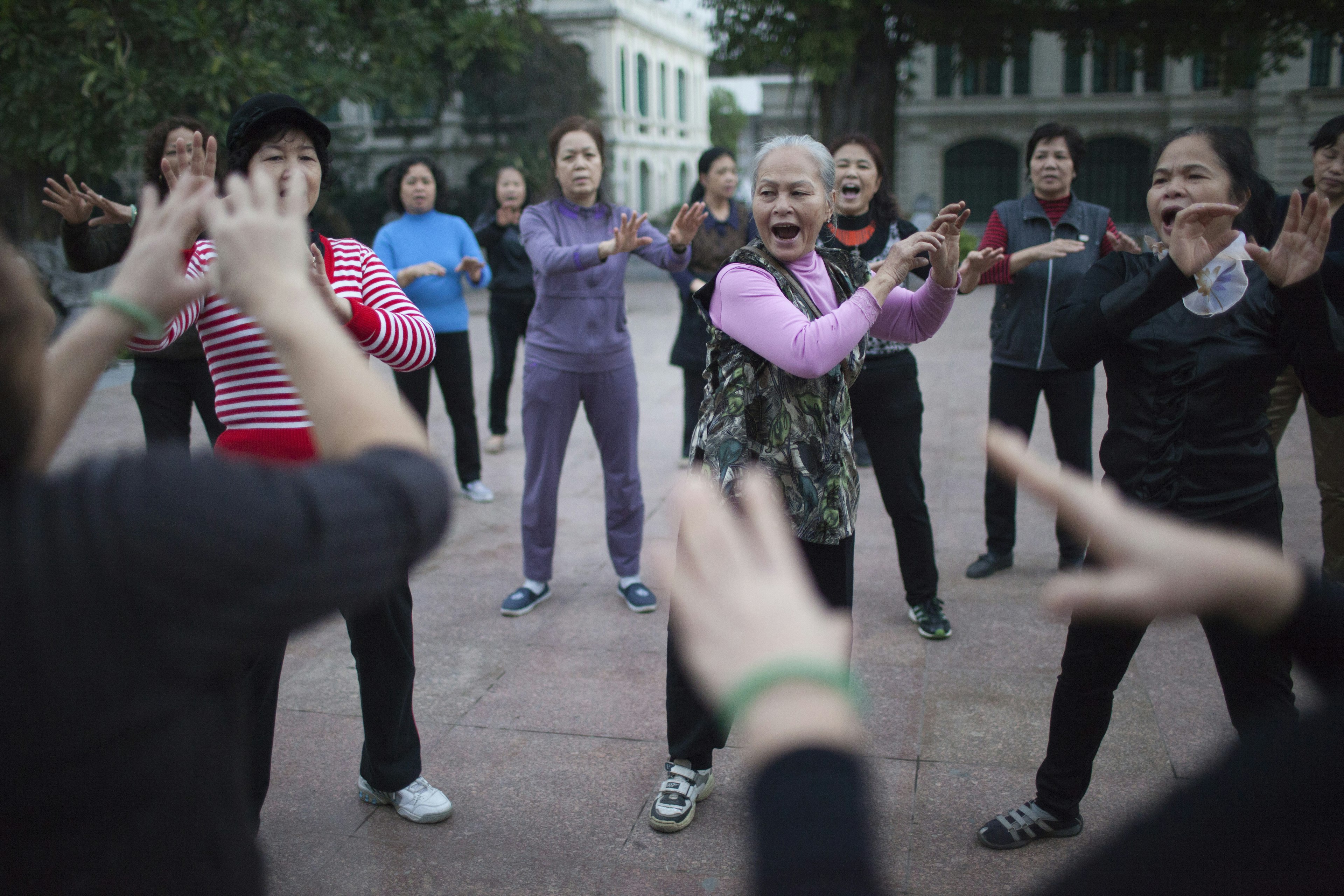 Women practice an exercise routine called "Laughing Yoga" in the early morning in Ly Thai To Square, Hanoi, Vietnam